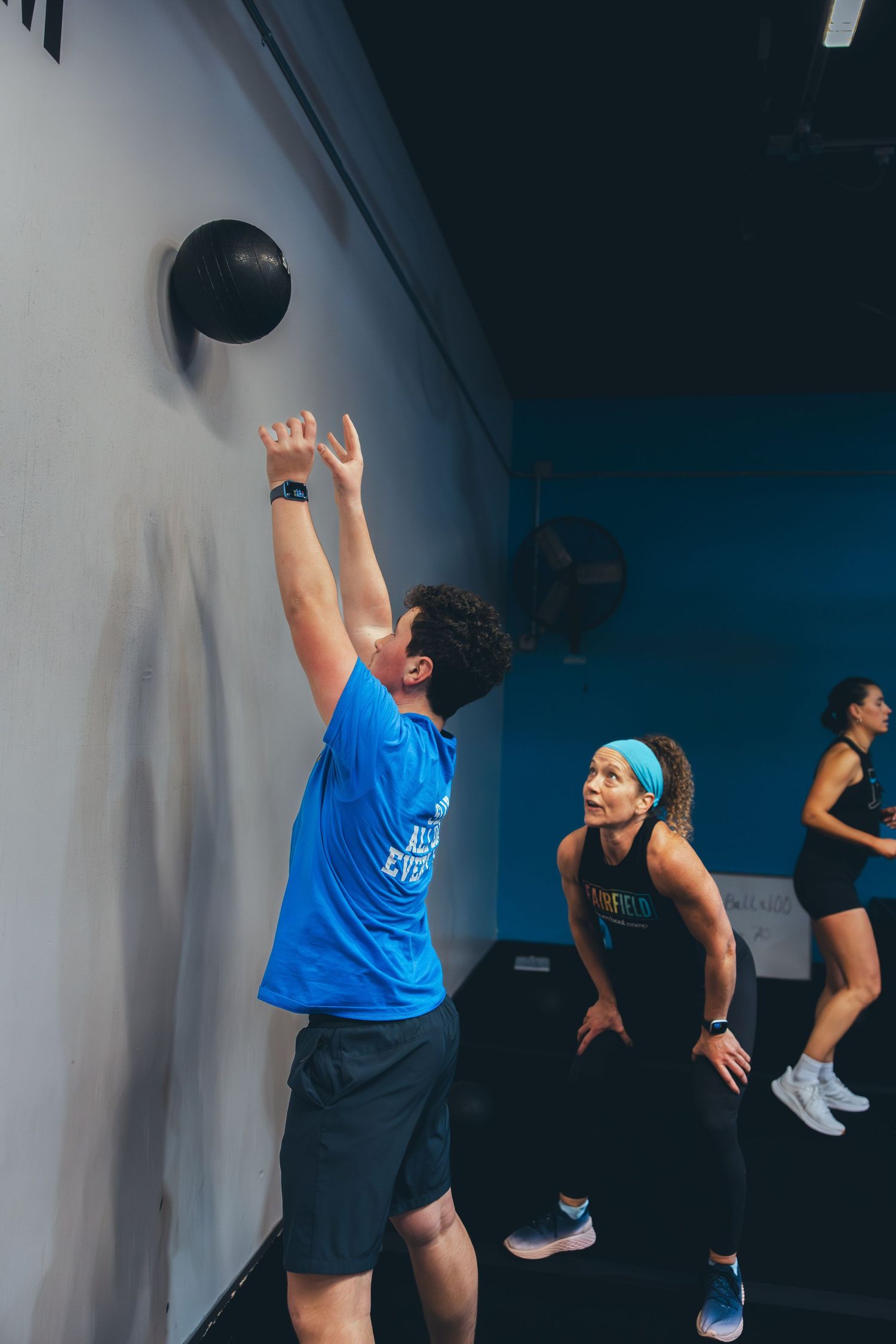 Participants perform wall ball exercises during a group workout session in a modern gym setting.