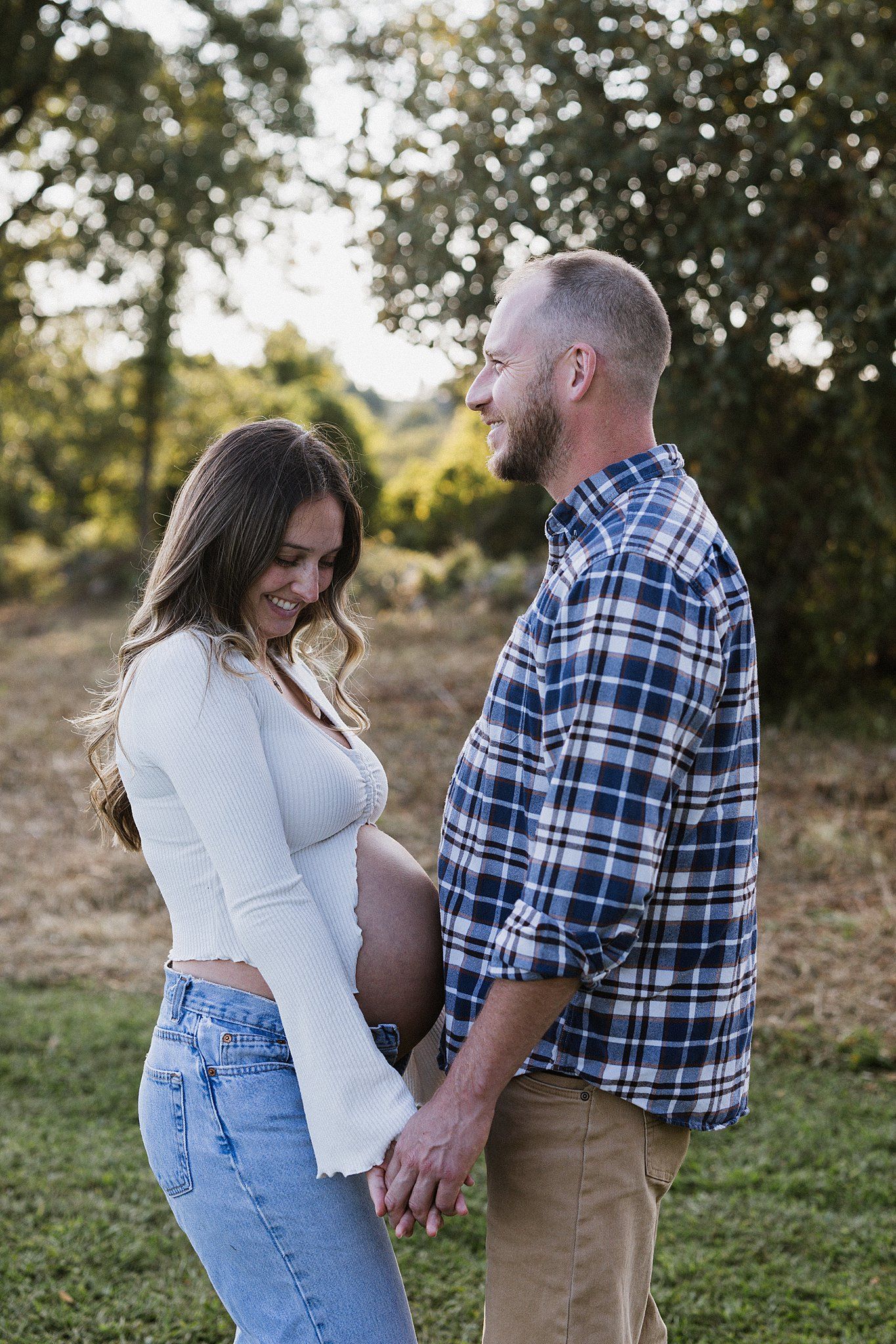 Expecting couple sharing intimate moment outdoors in casual clothing.