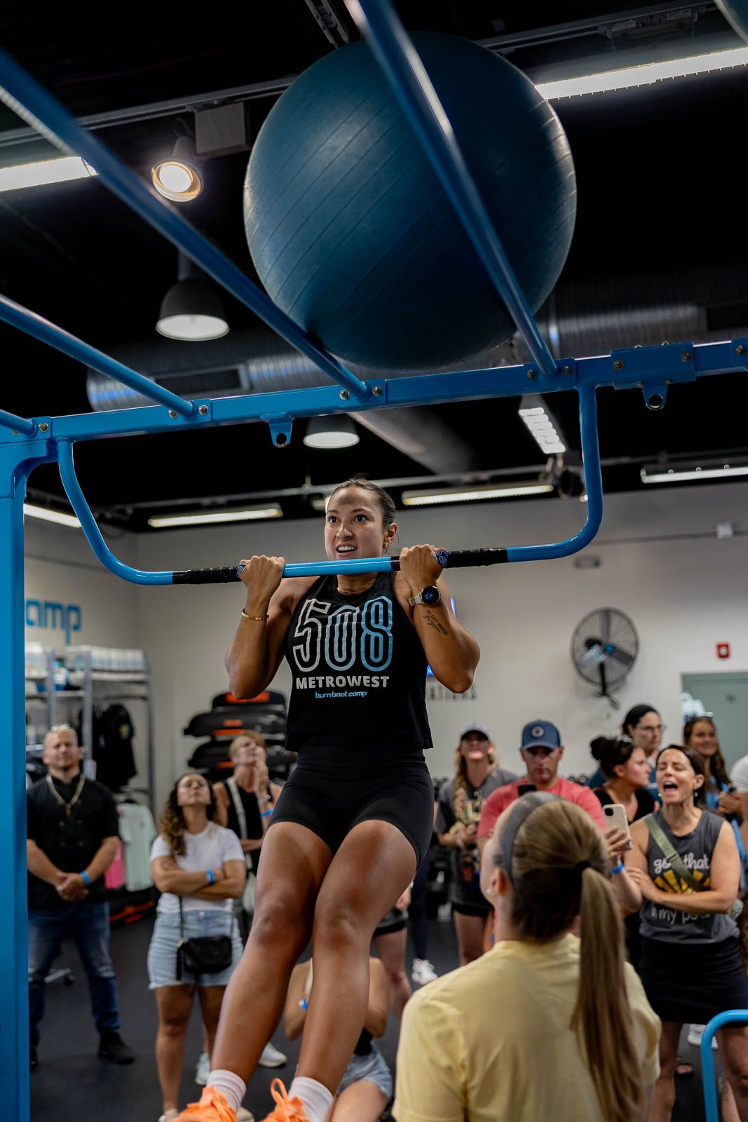 Athletes performing pull-ups on blue equipment during a group workout session in an indoor gym.