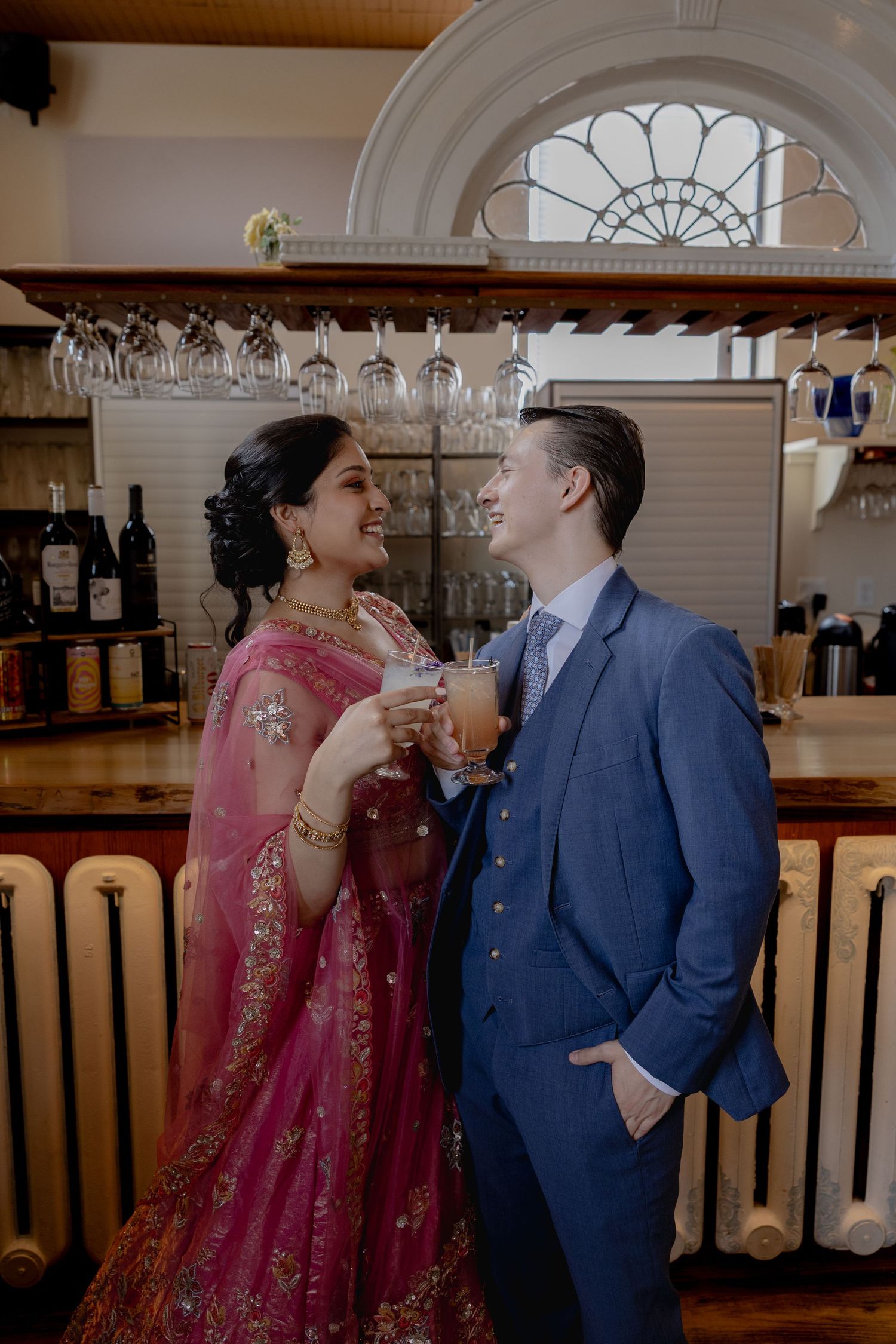 A couple in formal attire shares a lighthearted moment while standing at an elegant bar counter.