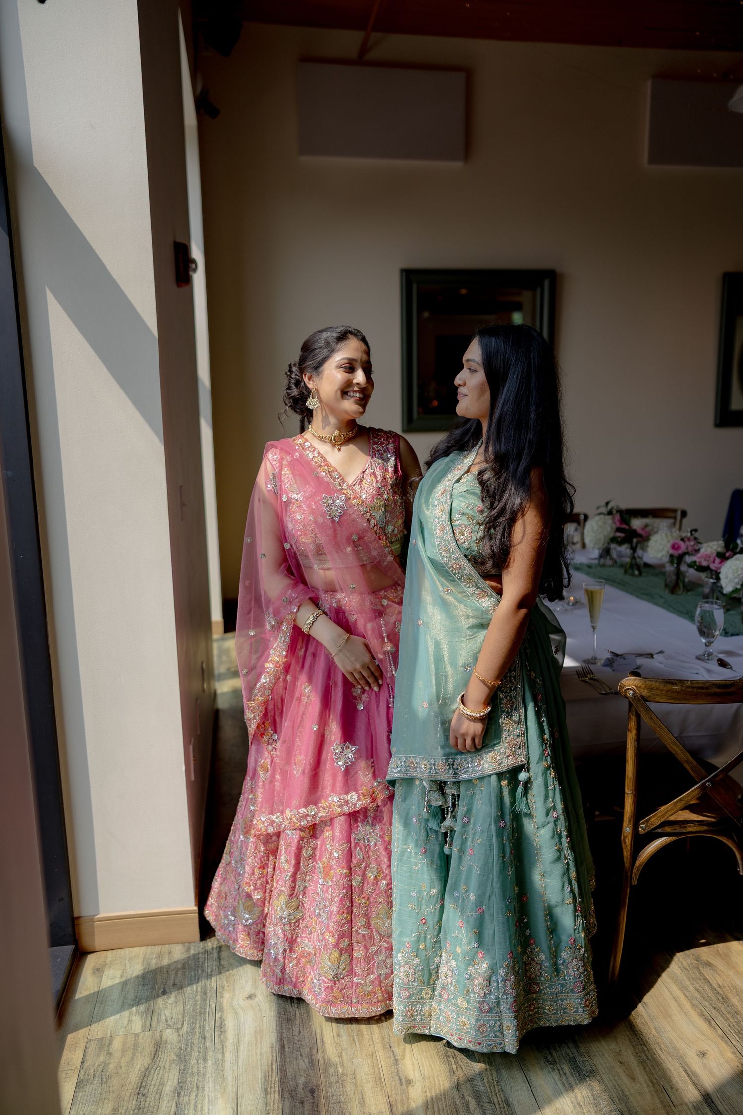 Two people in traditional Indian attire, one wearing pink and one in mint green, share a joyful moment together.