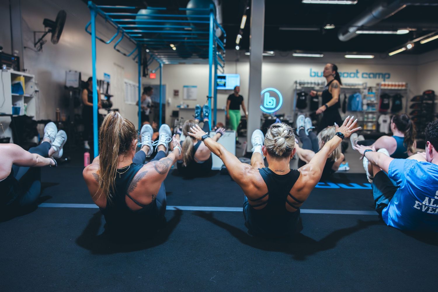 Fitness class participants performing synchronized floor exercises in a gym with blue equipment.
