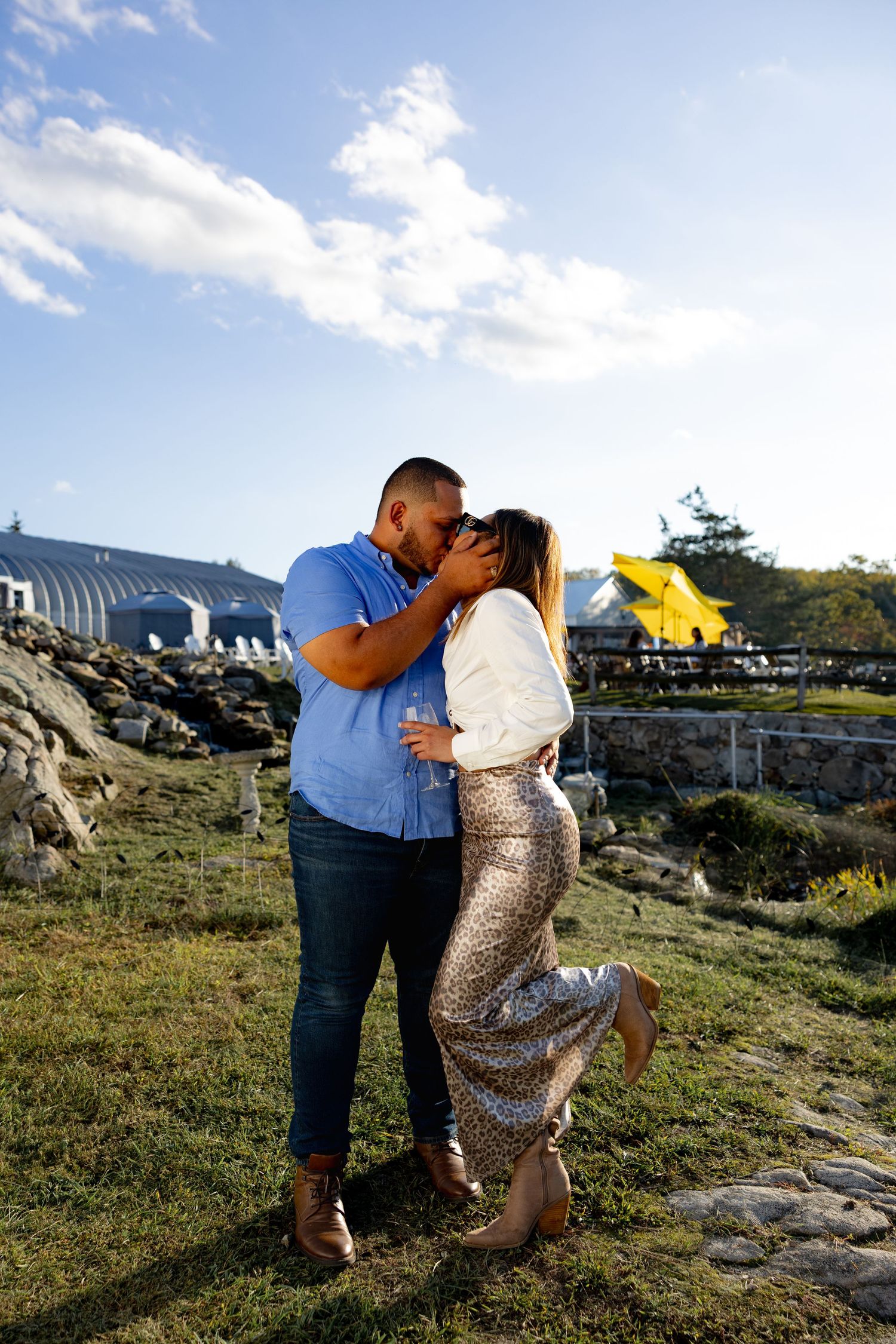 A romantic couple shares tender moments on a rocky coastal landscape during sunset with buildings in the background.