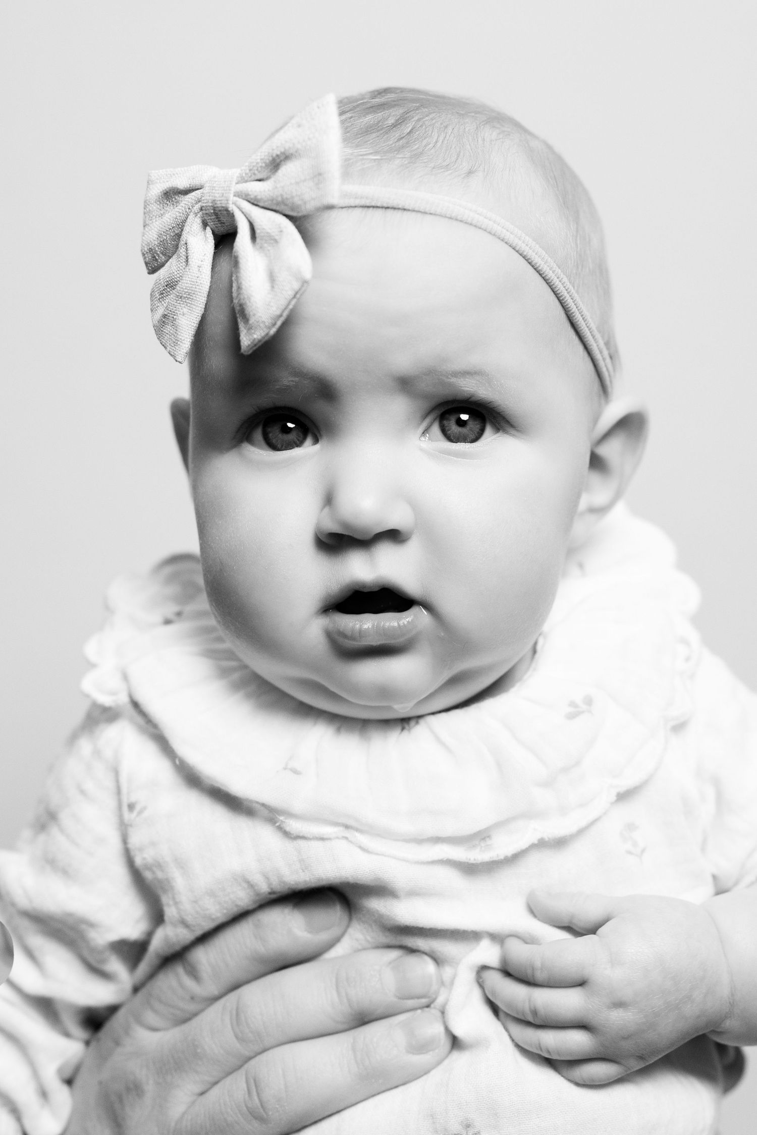 A series of black and white close-up portraits showing a baby wearing a white bow and ruffled collar.