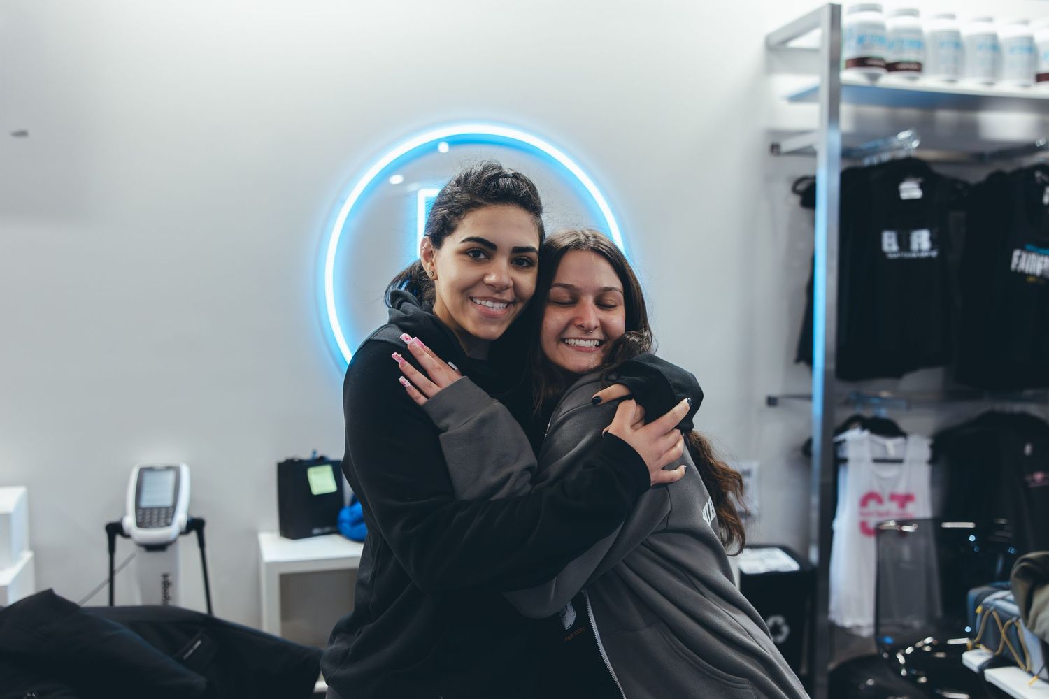 Two people sharing a warm embrace in a gym with blue neon lighting.