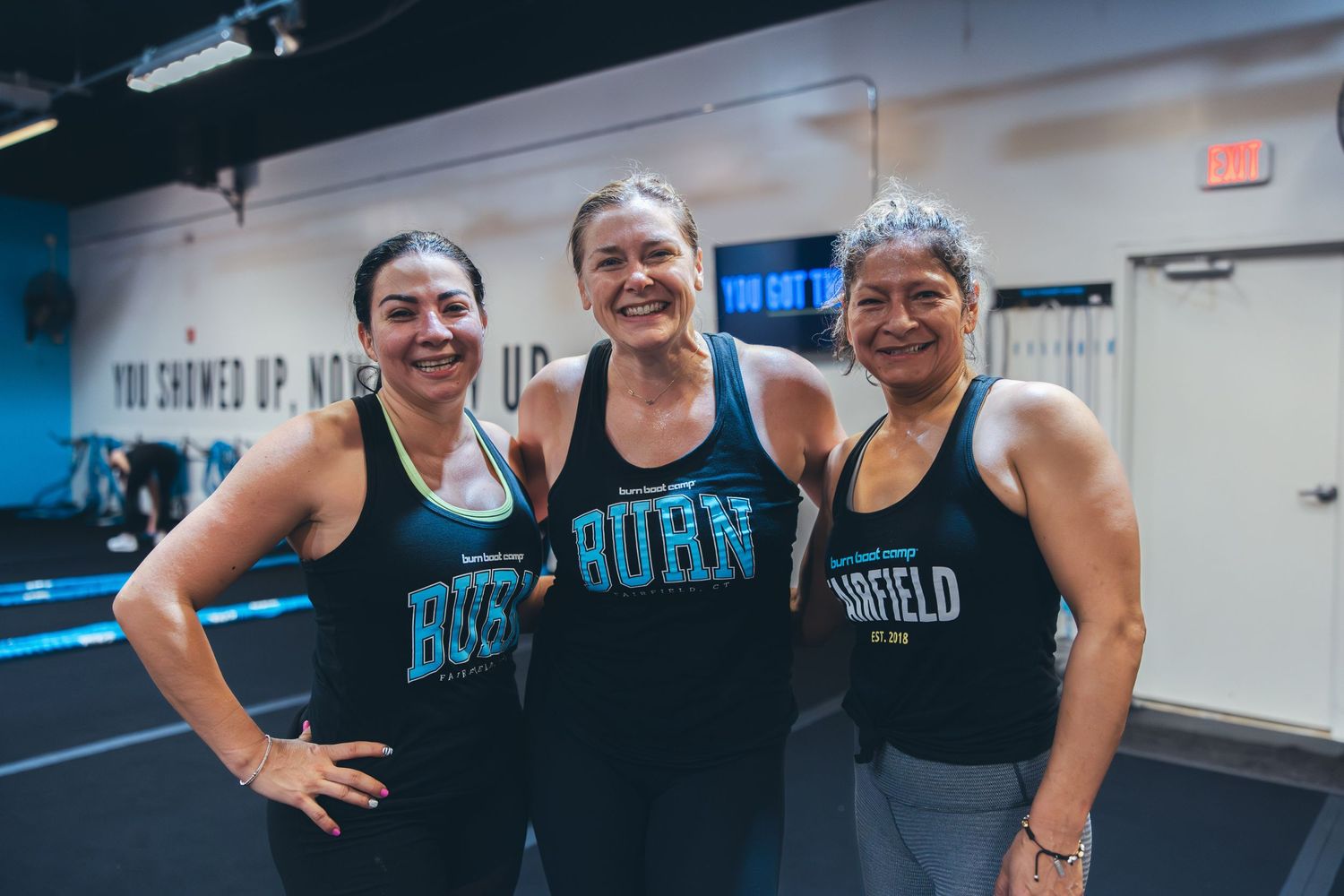 Three athletes in matching BURN tanks standing together in a gym setting.