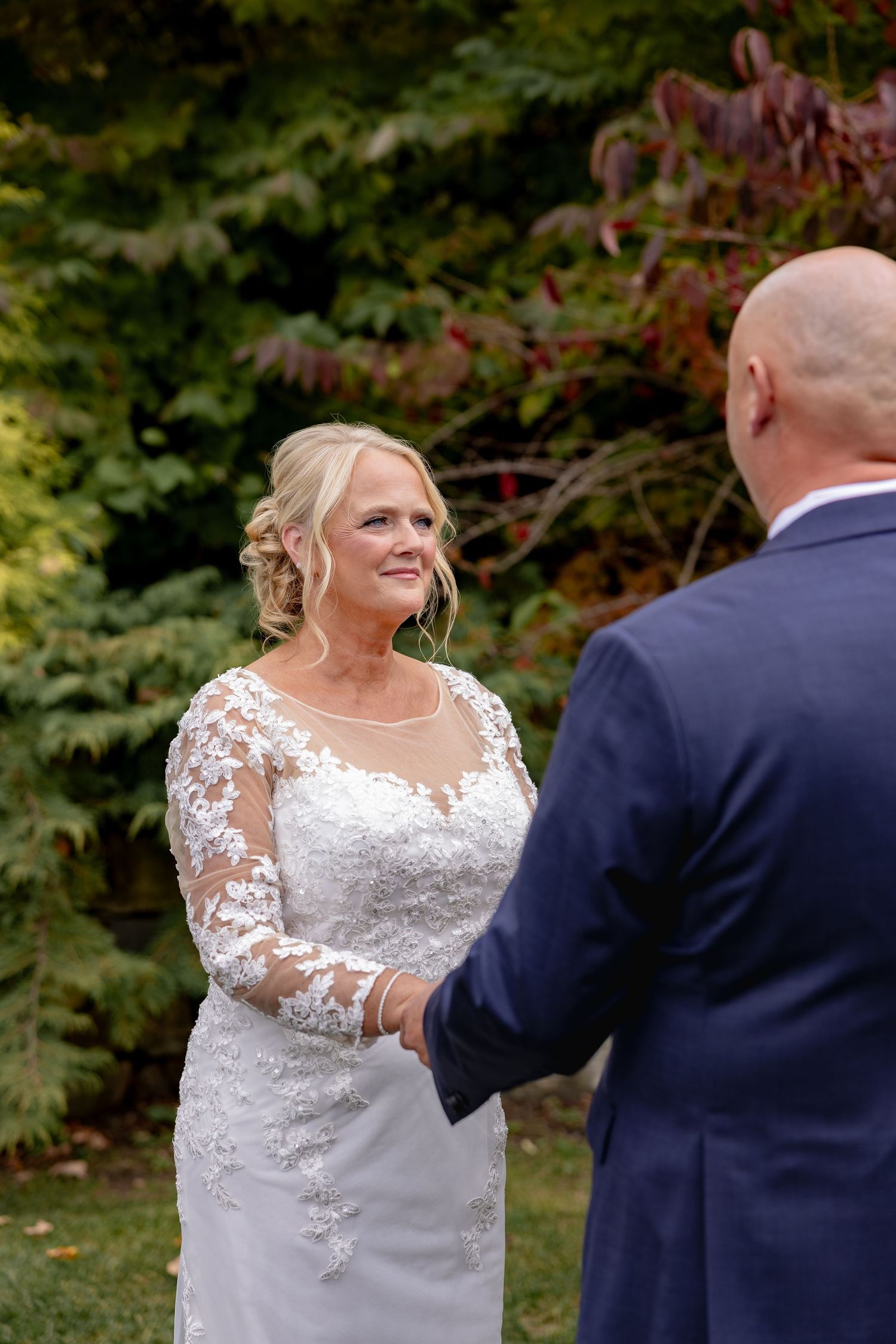 A bride and groom share their first look moment in a garden setting with fall colors in the background.