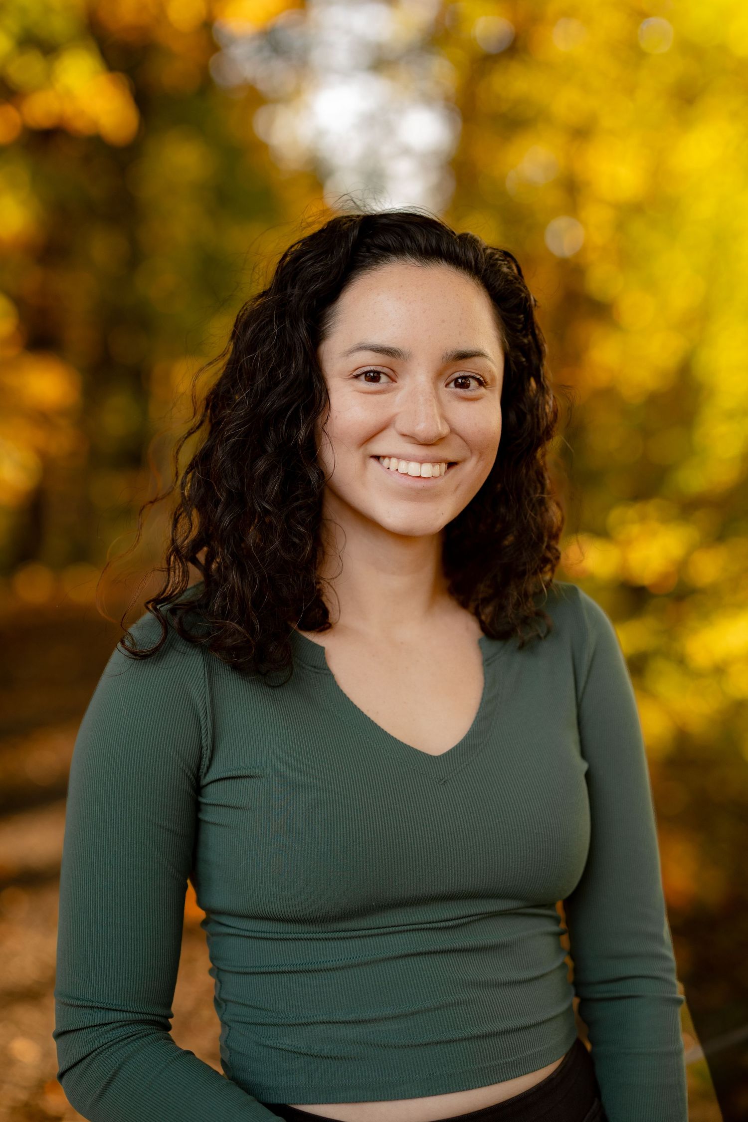 Portrait series in autumn showing a person in a dark green top against vibrant yellow foliage background.