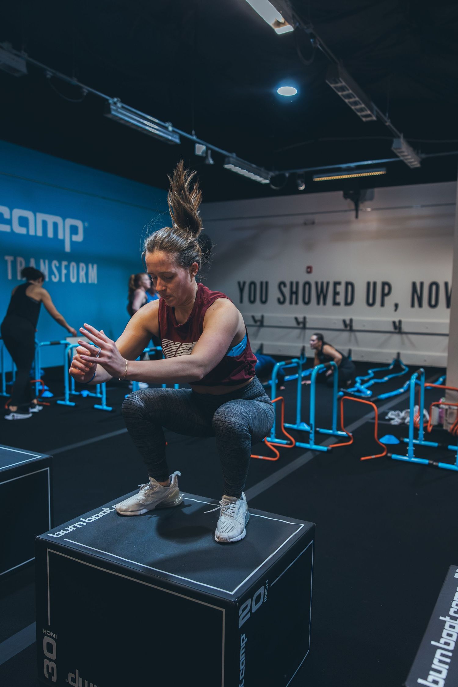 Athlete performing box jump exercise in modern gym with motivational wall text.