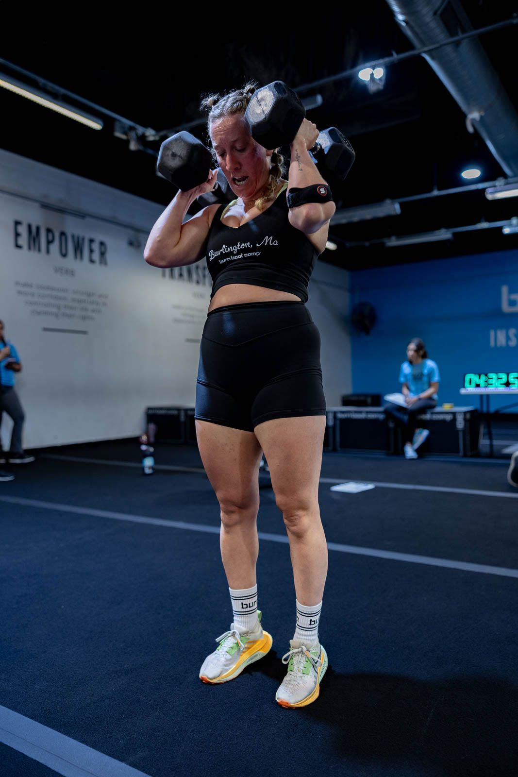 Strong athlete performing shoulder presses with dumbbells in a gym with 