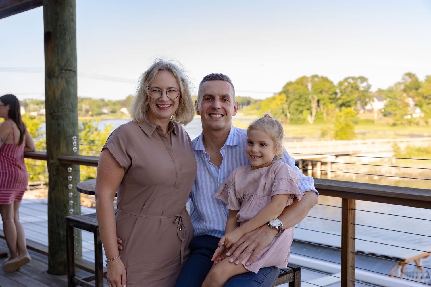 People enjoying a sunny day together on a wooden deck overlooking water.