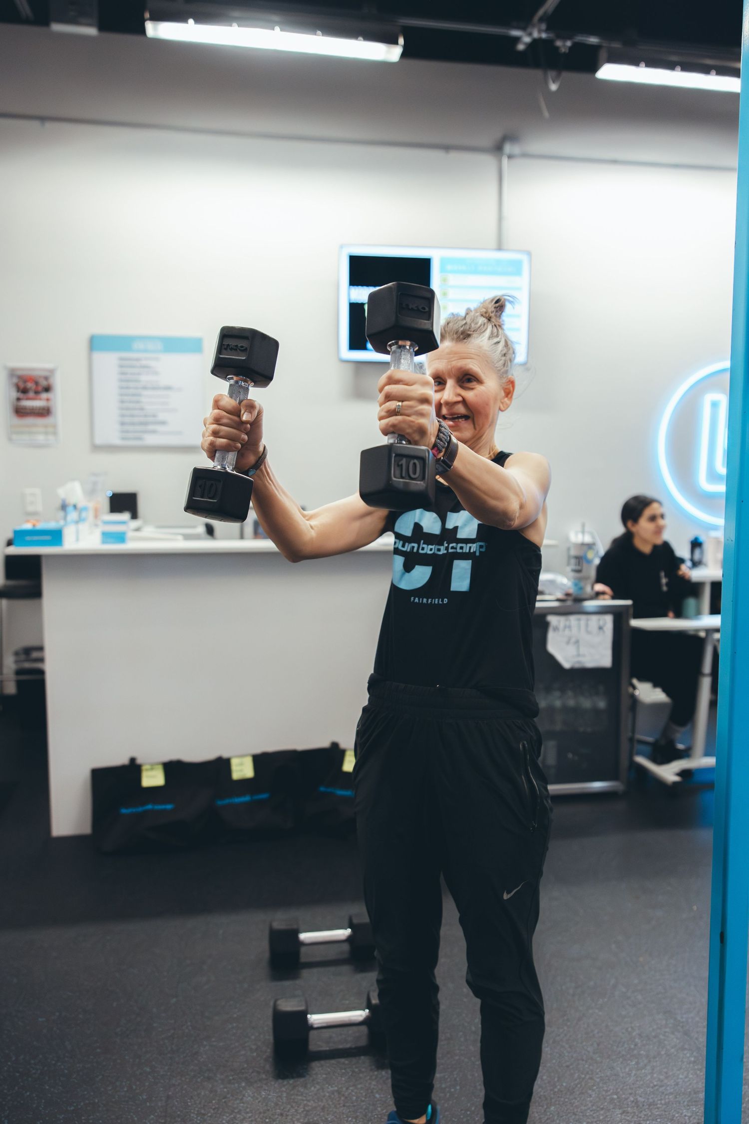 Person in workout attire holding dumbbells overhead with enthusiasm.