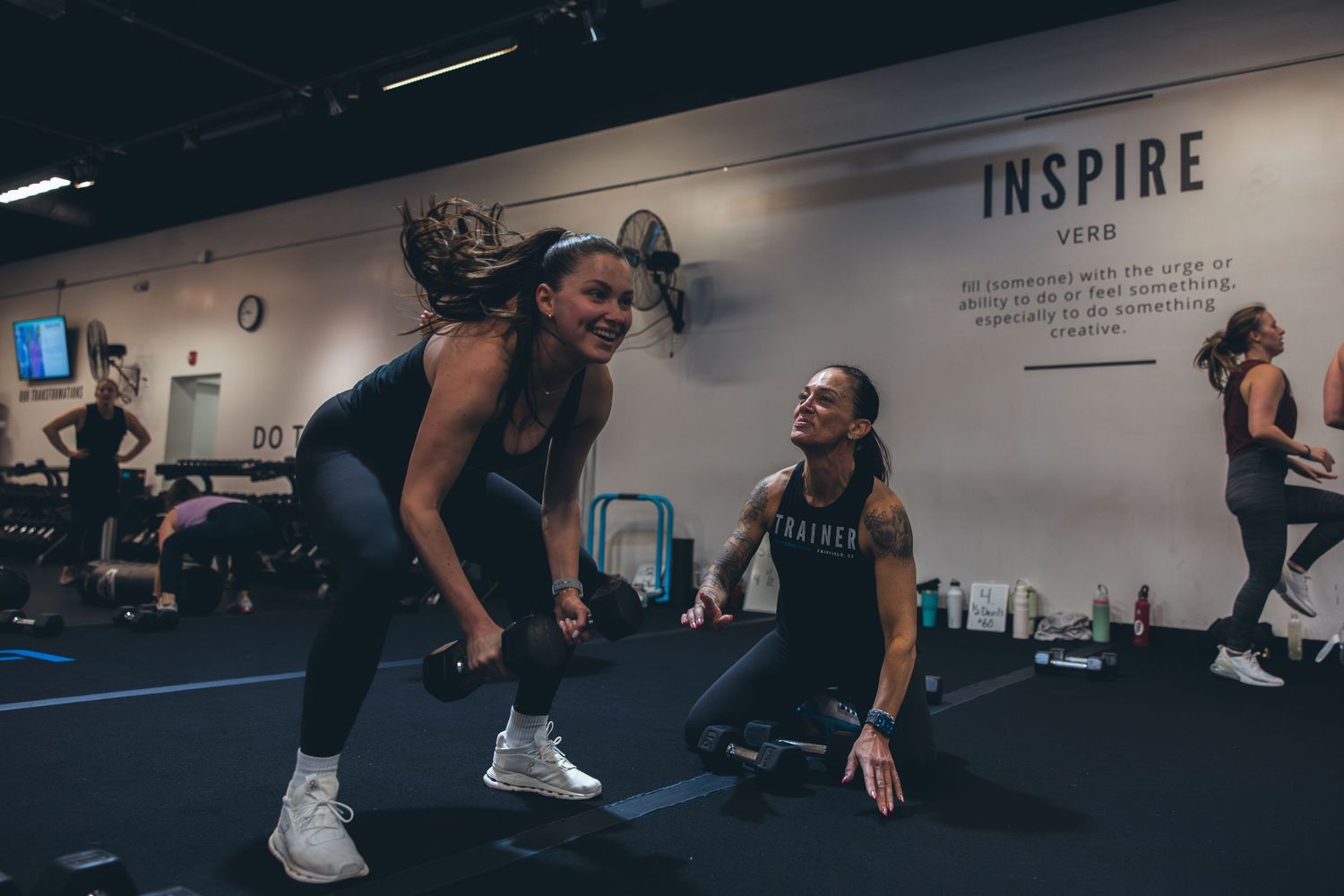Group fitness class participants working out together in a dark studio with inspirational wall text.