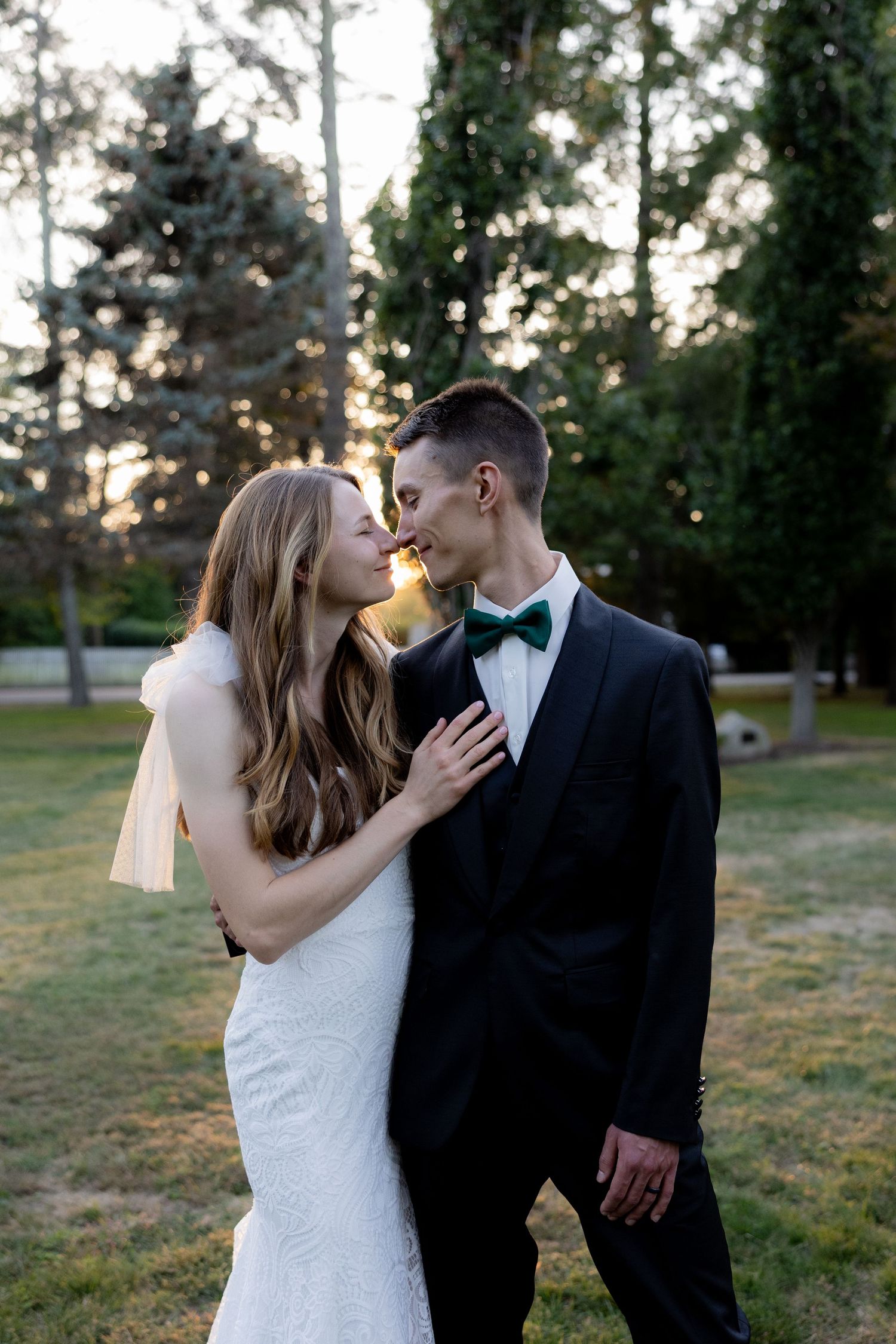A romantic wedding couple shares intimate moments in a park at sunset as golden light filters through trees.
