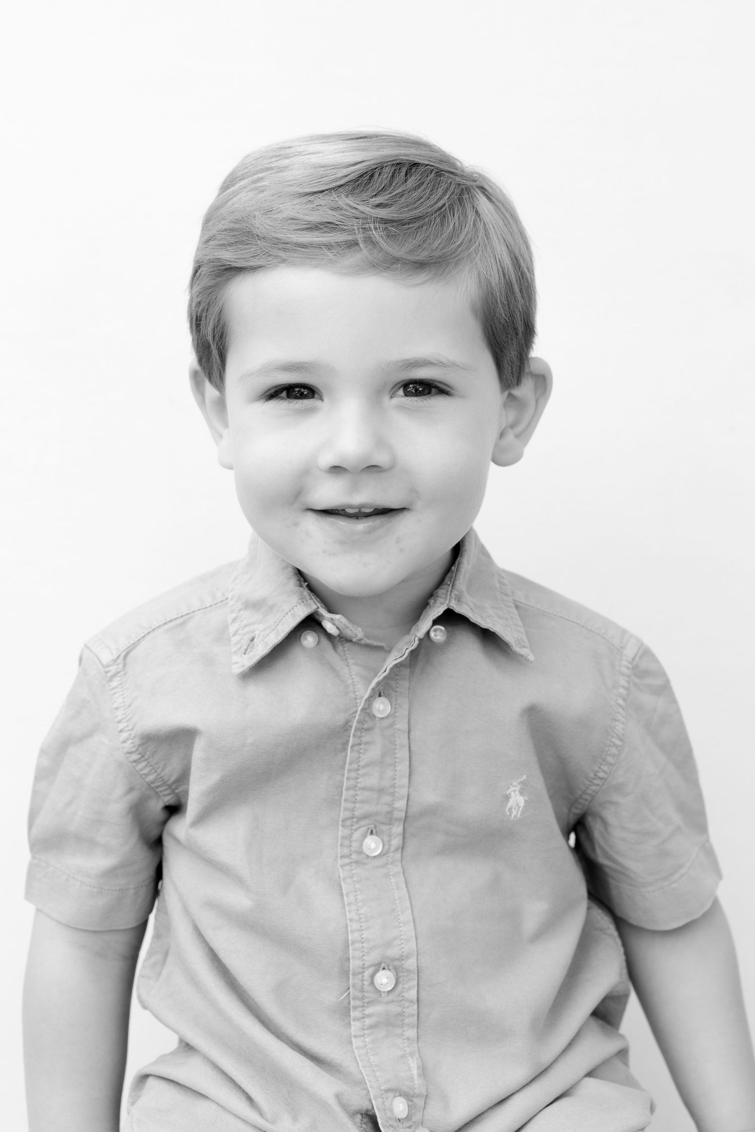A young child in a light colored button-down shirt poses in a series of four similar photos.