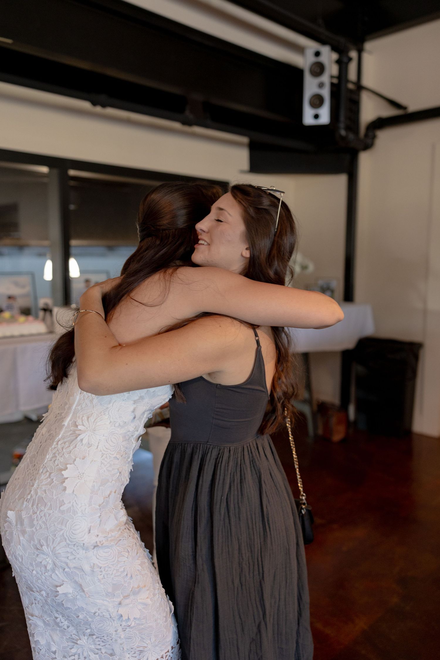 Two people embrace warmly in a room with hardwood floors and industrial-style lighting.