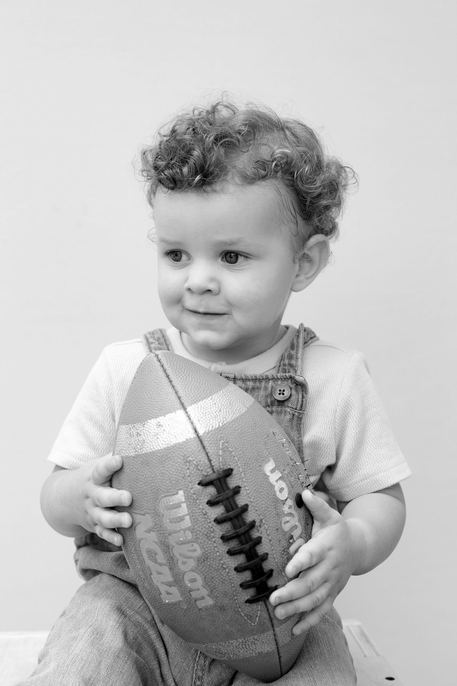 Black and white photo series of a baby in white clothing holding a football, shown from different angles.