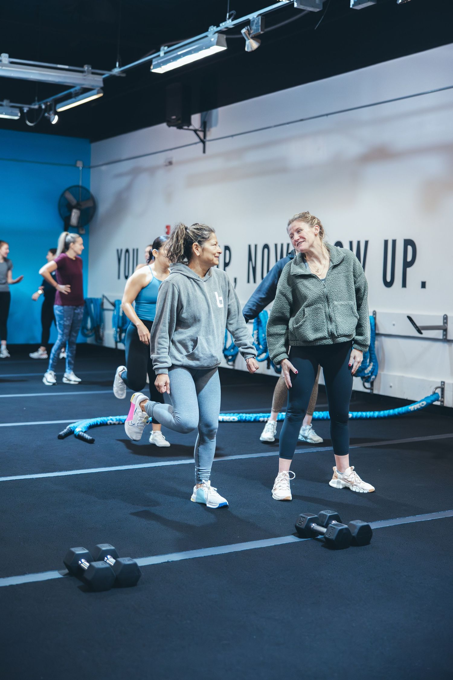 Women working out in fitness class at modern gym with blue walls.
