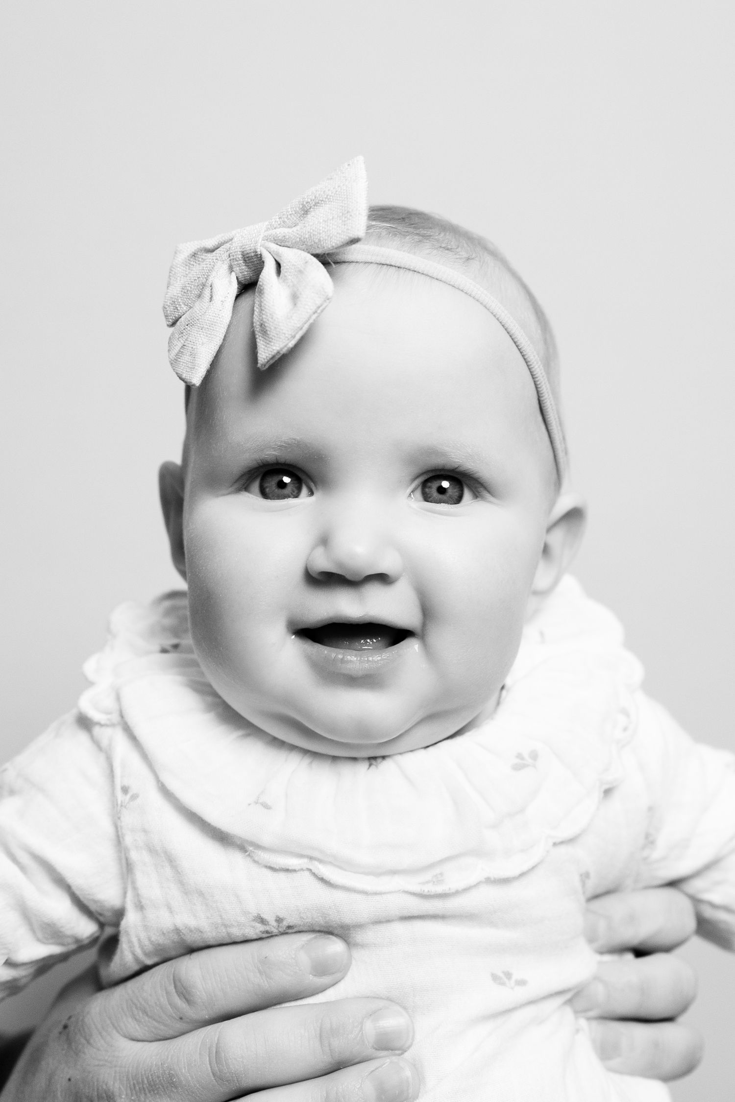 A series of black and white portraits showing a baby in white clothing with small hair bows smiling at the camera.