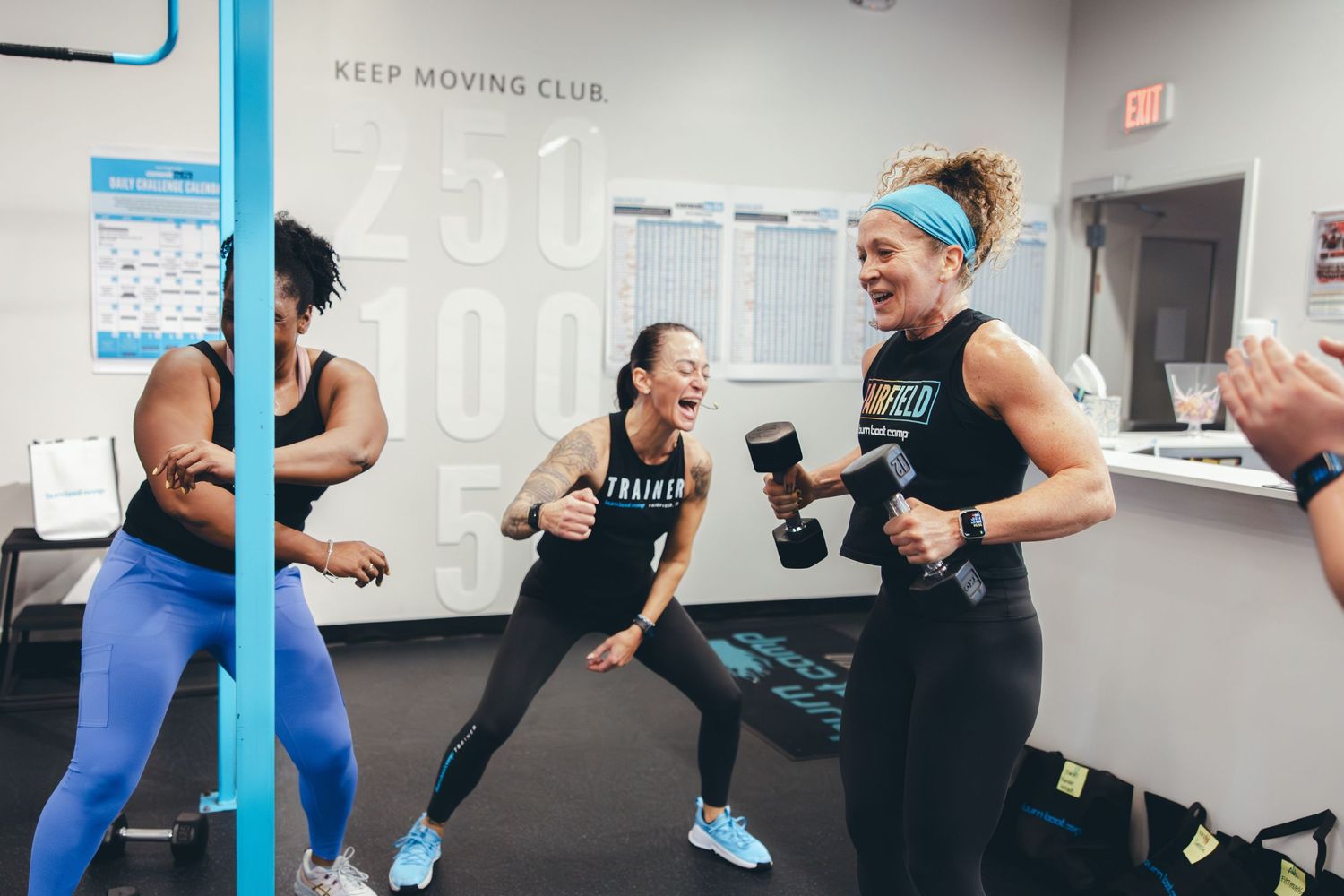 Lively group fitness session with participants exercising with dumbbells in a bright studio space.
