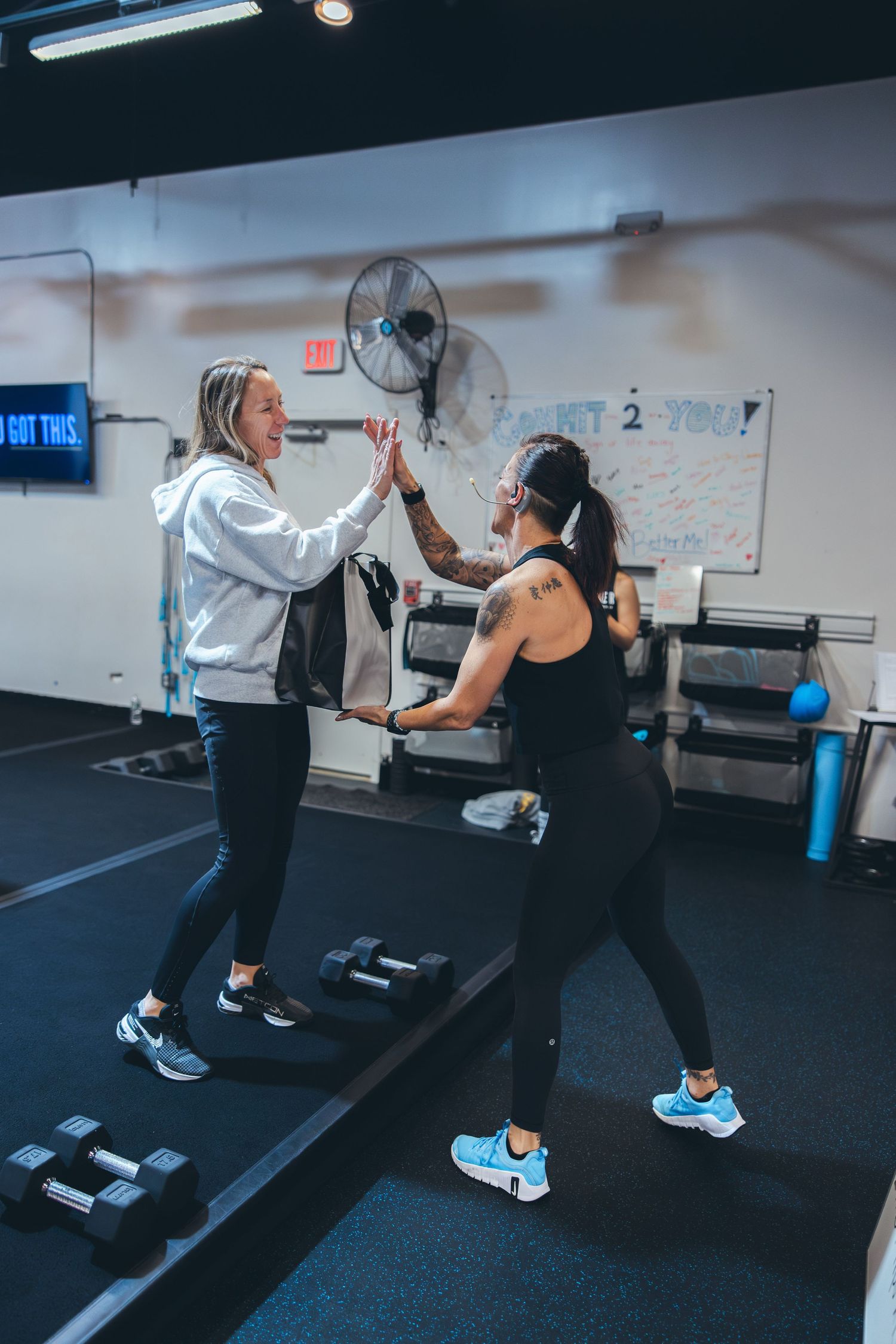 Two workout partners high-fiving during fitness training session in gym with dumbbells on floor.