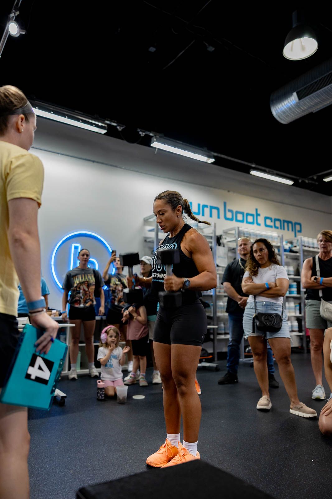 Fitness class participants performing squats and exercises in a modern gym with blue wall accents during a workout session.