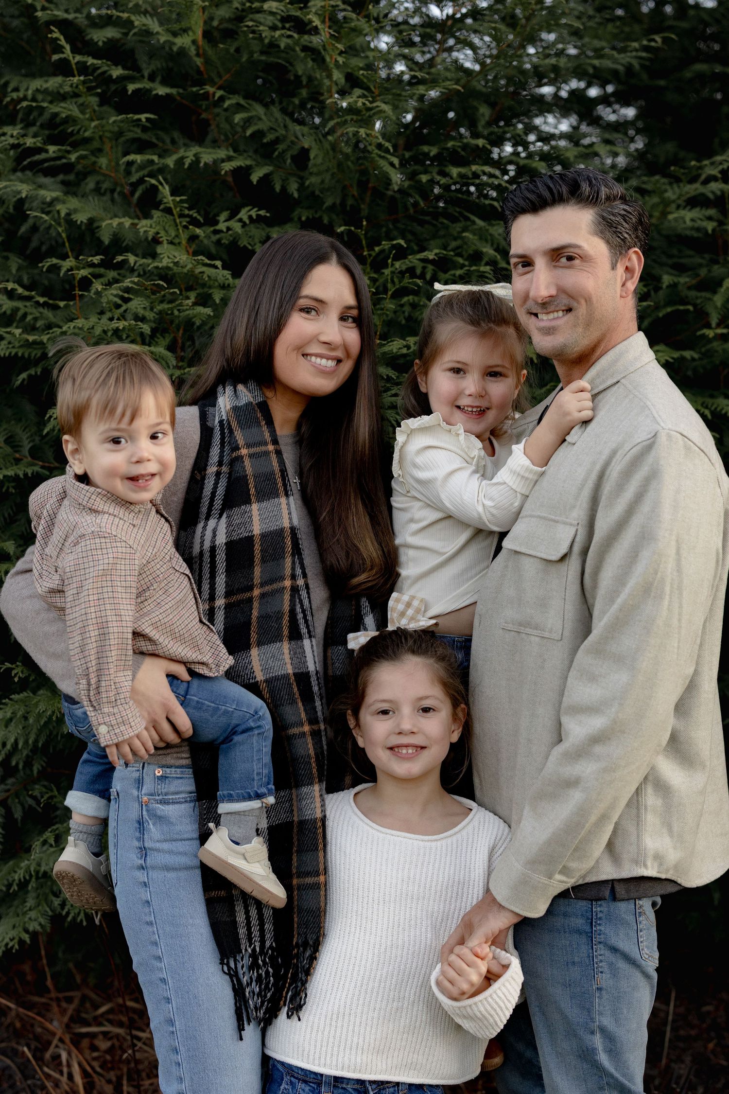 A family wearing casual attire poses together against an evergreen backdrop in a series of candid outdoor portraits.