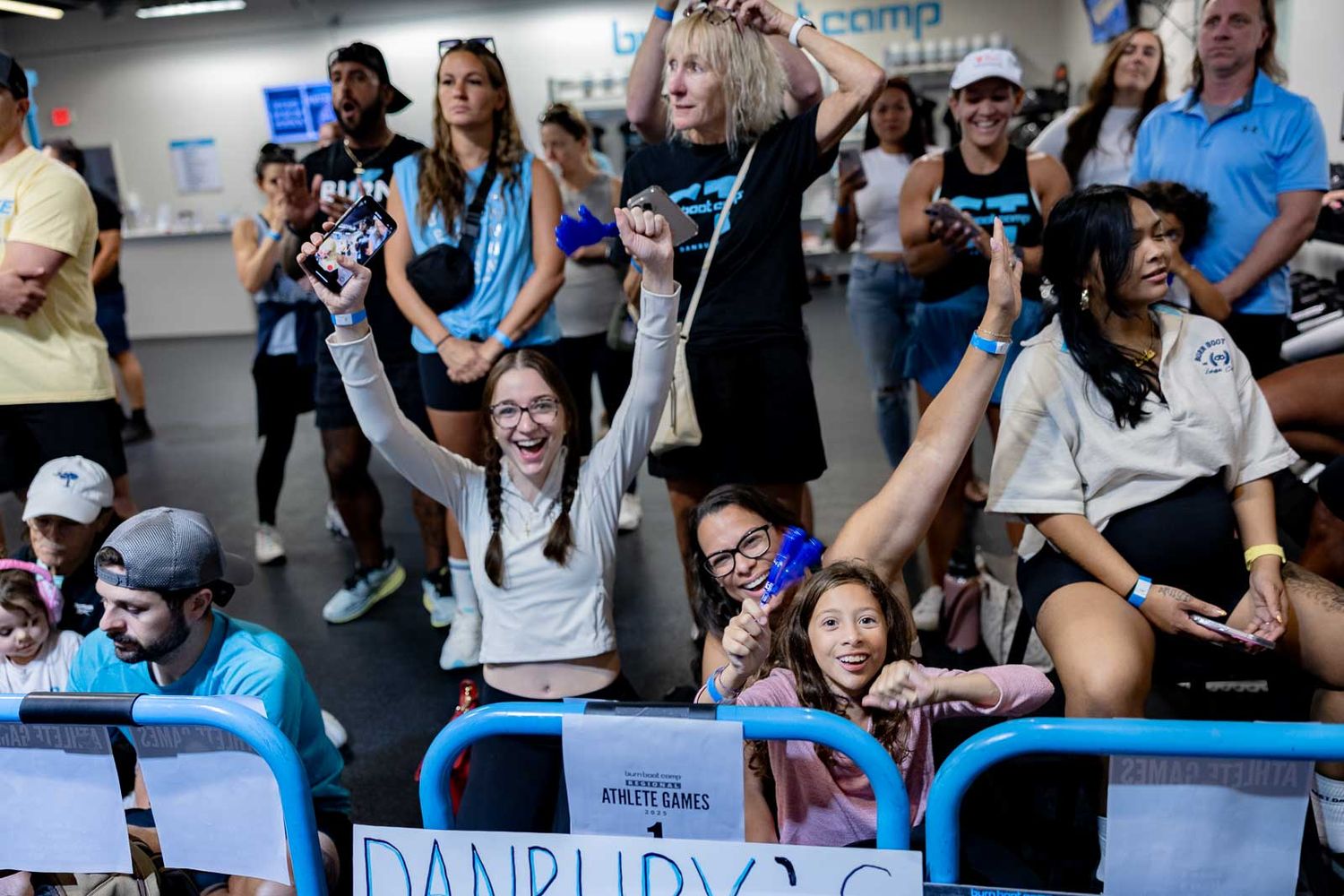 Enthusiastic crowd cheers and celebrates during a high-energy fitness event in a training facility.