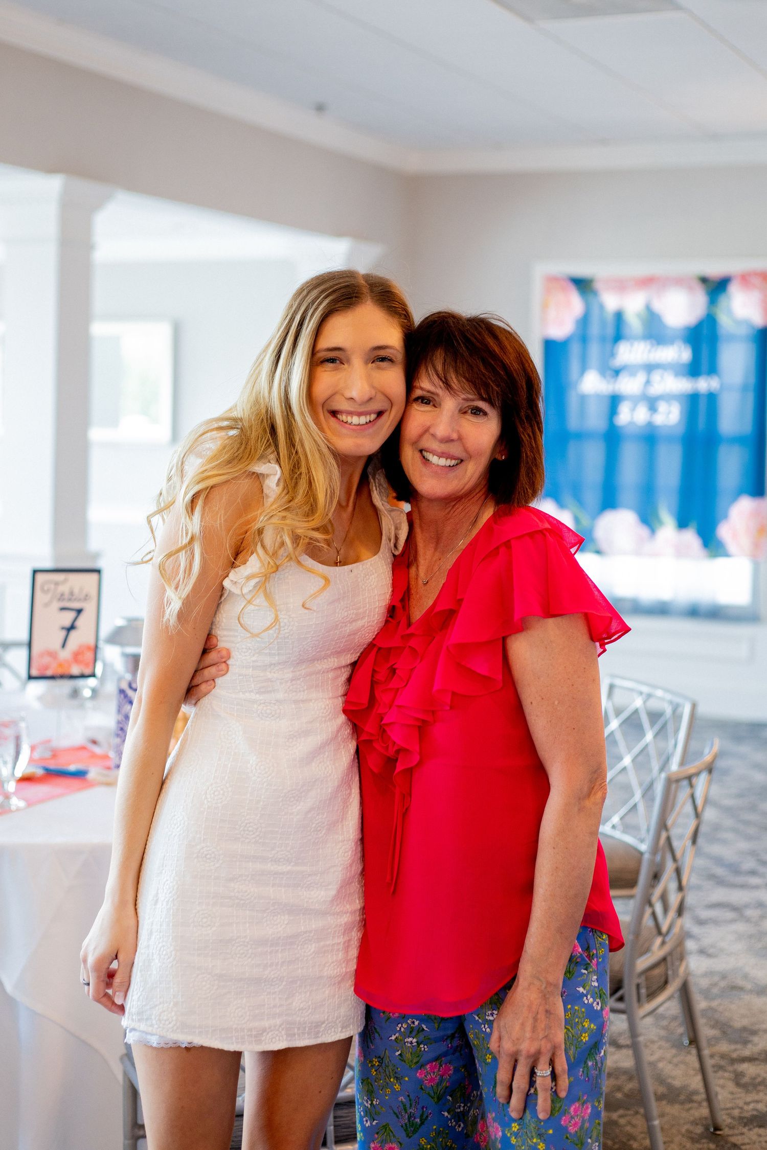 Two women pose together at an indoor event, one wearing white and one in bright red.