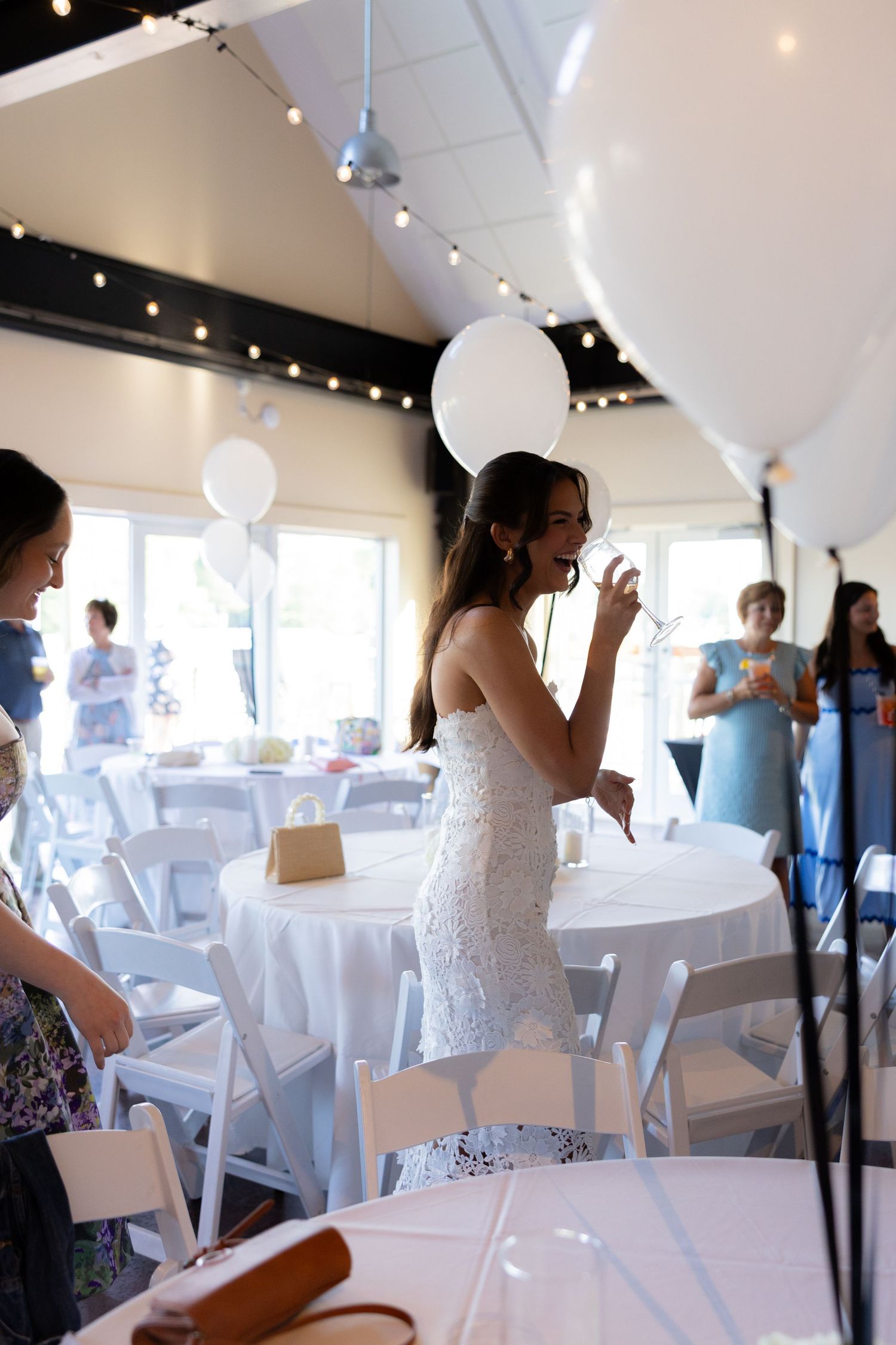 Guests celebrate at an elegant indoor reception venue with white tables and modern lighting.