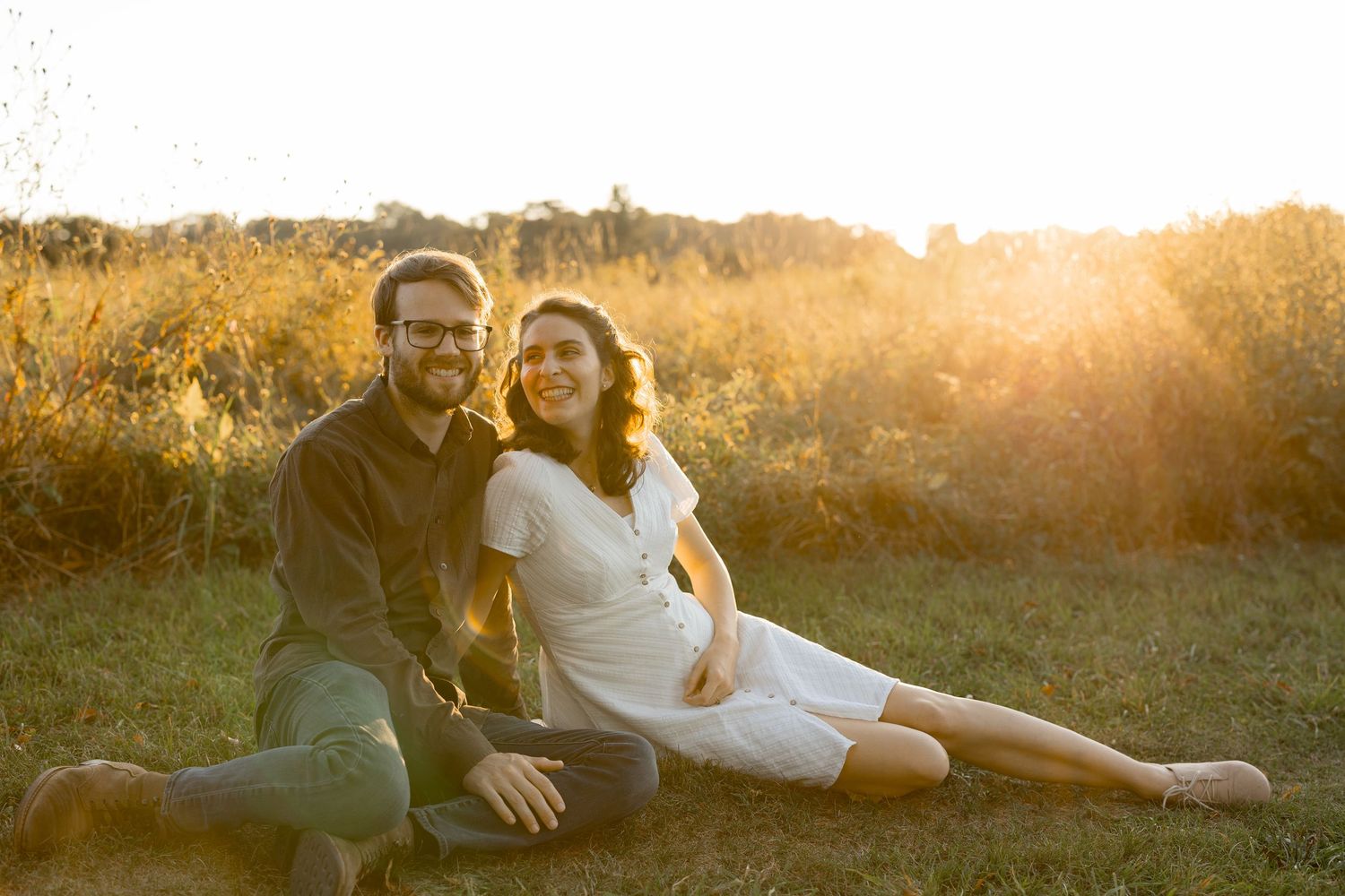 Couple lying in a golden sunlit meadow during sunset while sharing an intimate moment together.