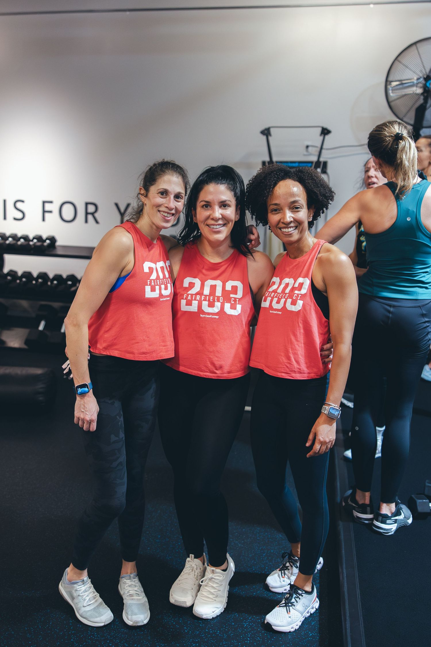 Group of athletes wearing matching red workout tops pose together at fitness studio.