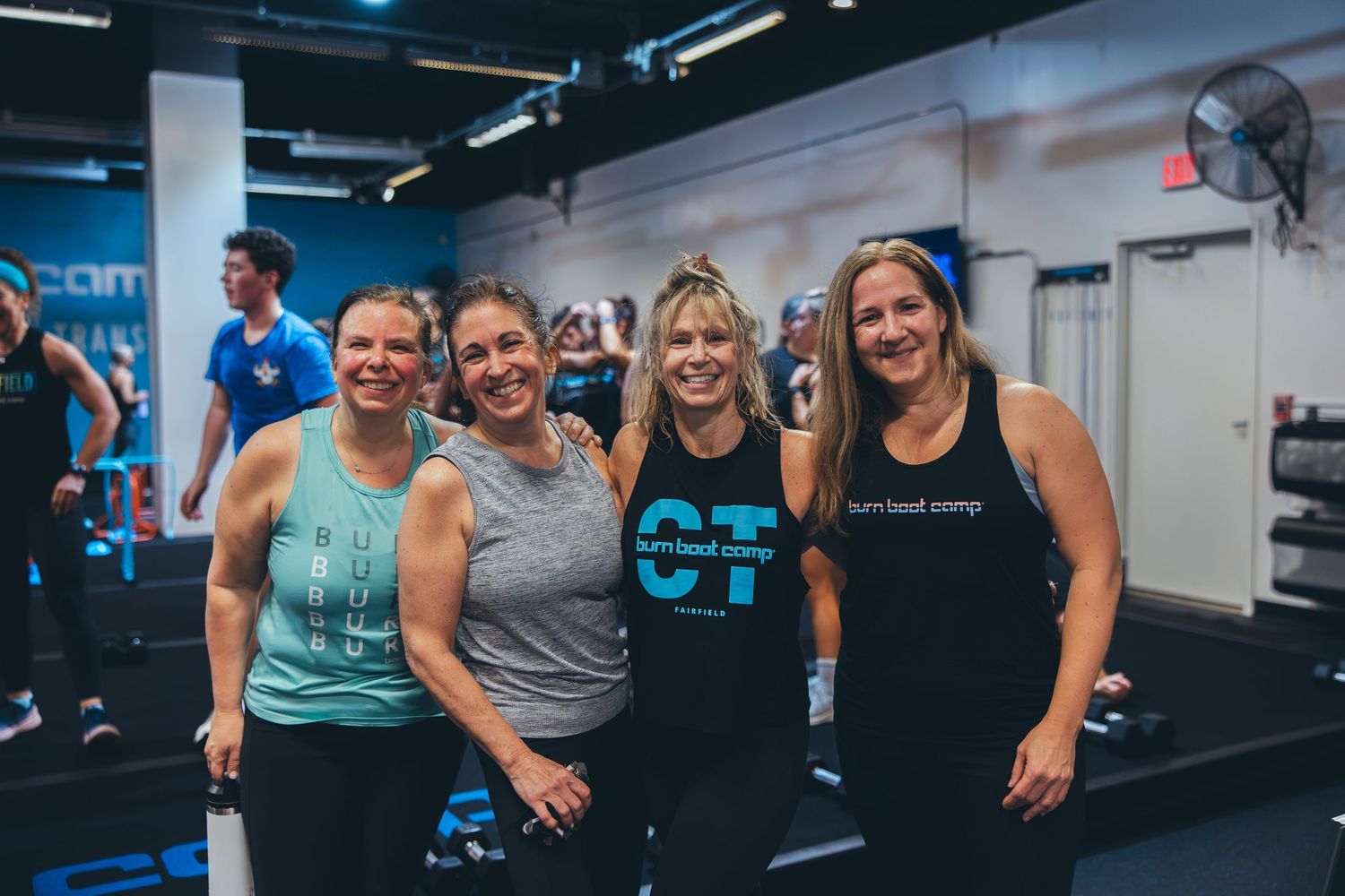 Group of energetic fitness instructors posing together at Burn Boot Camp facility.