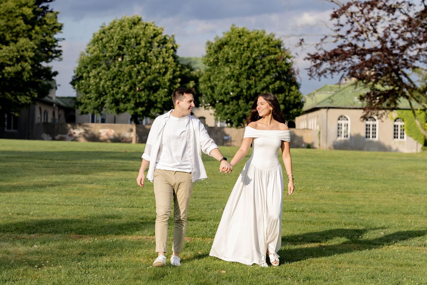 A couple in wedding attire walks together across a lush green lawn on their special day.