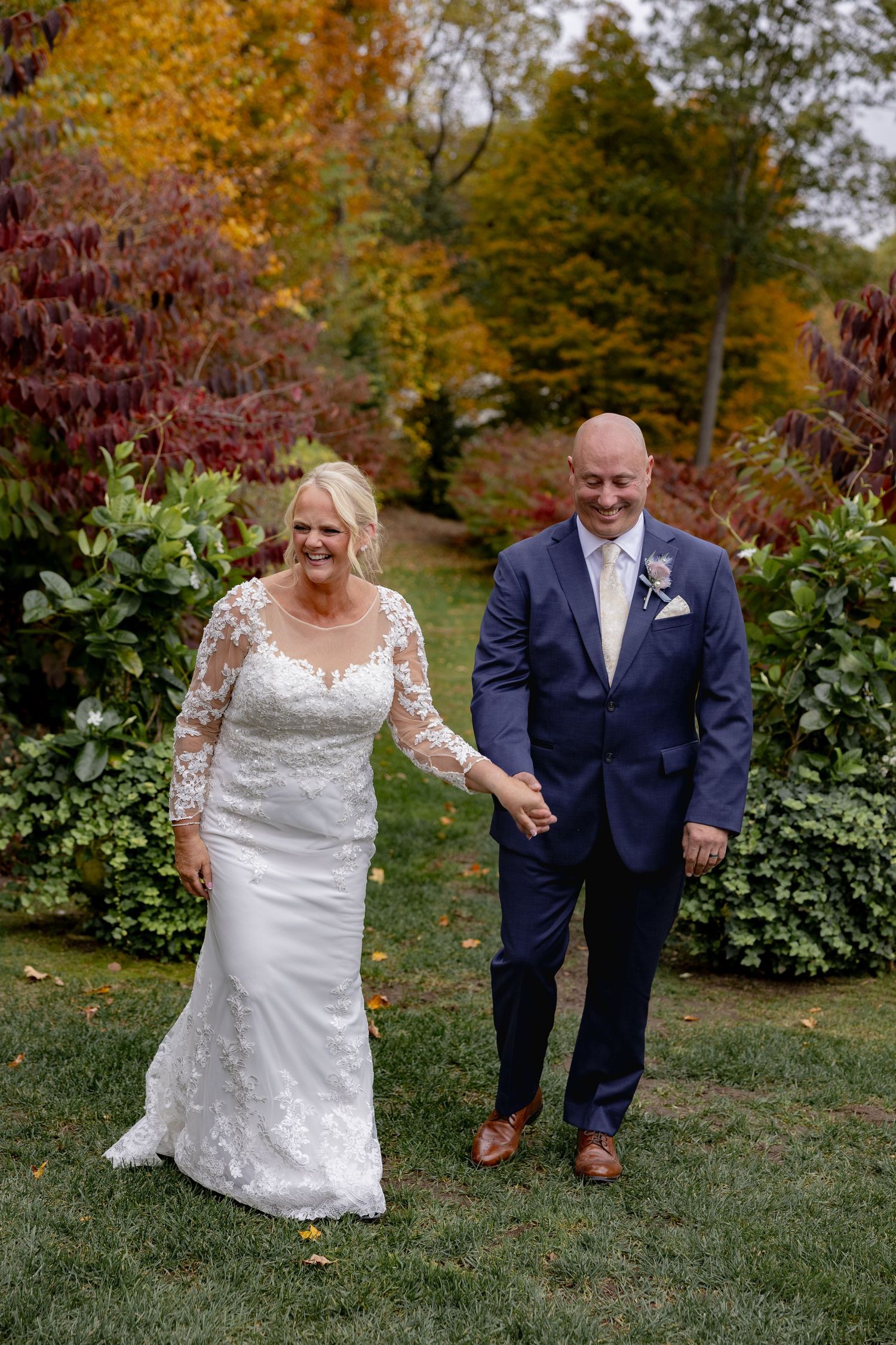 Couple shares joyful moments together on their wedding day surrounded by vibrant autumn foliage in a garden setting.