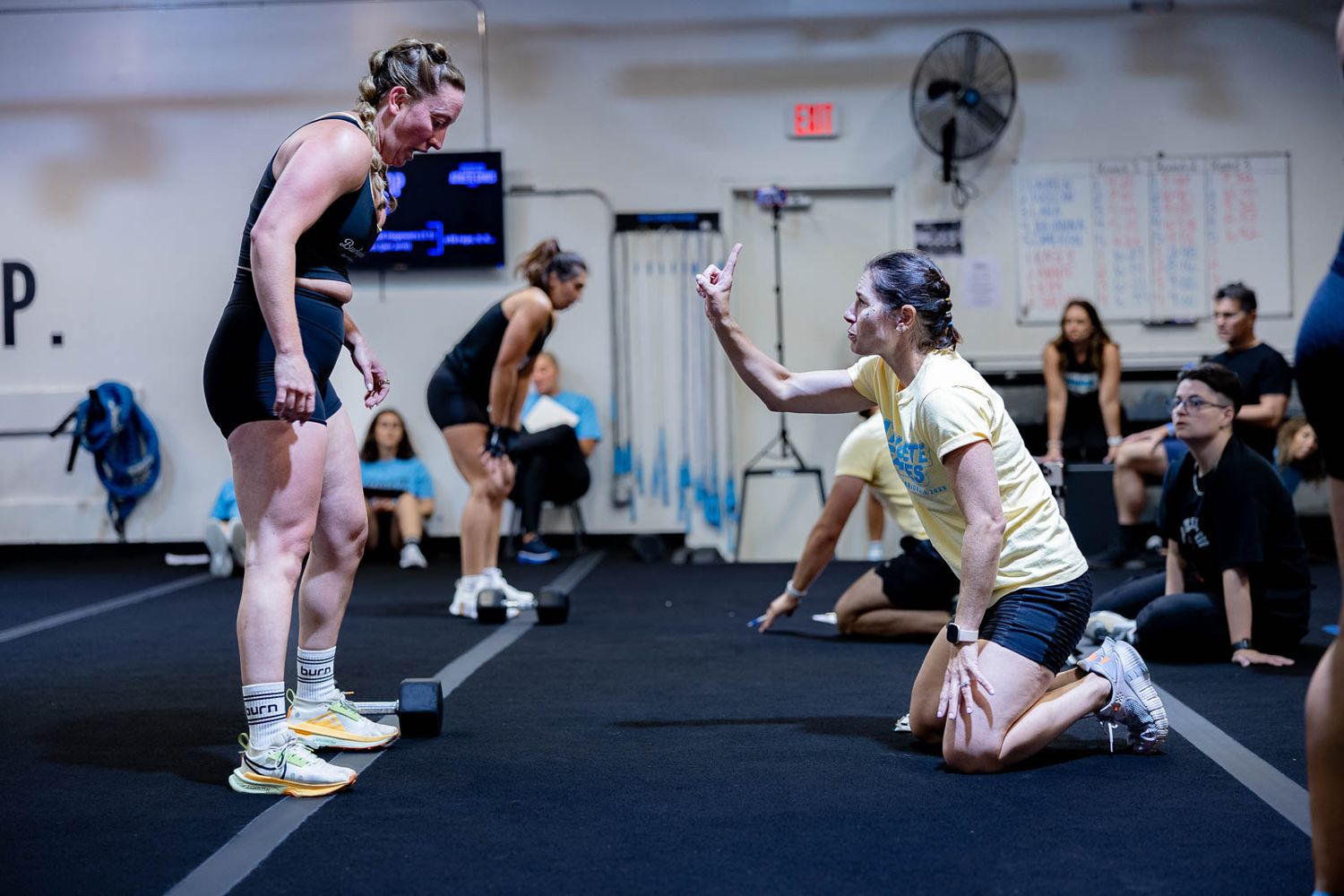 Exercise coach providing instruction and guidance to participants during a CrossFit workout session in a fitness gym.