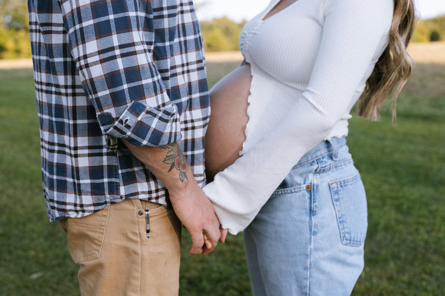 Close-up of expectant couple holding hands in a park setting.