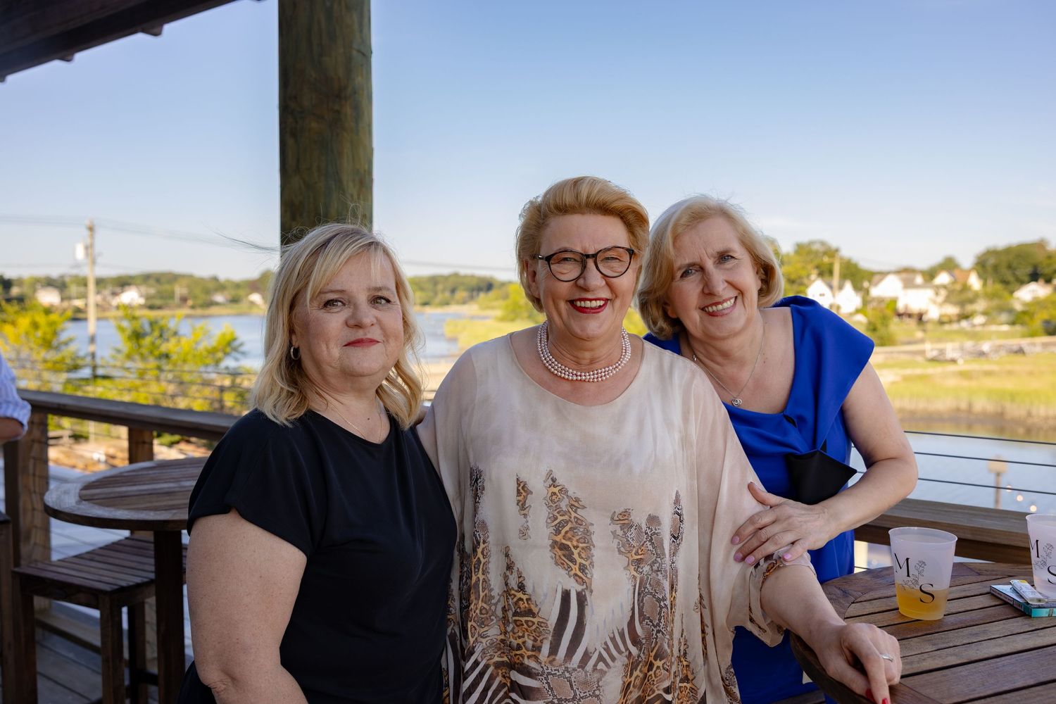Group enjoying drinks and conversation on an outdoor waterfront deck during sunset.