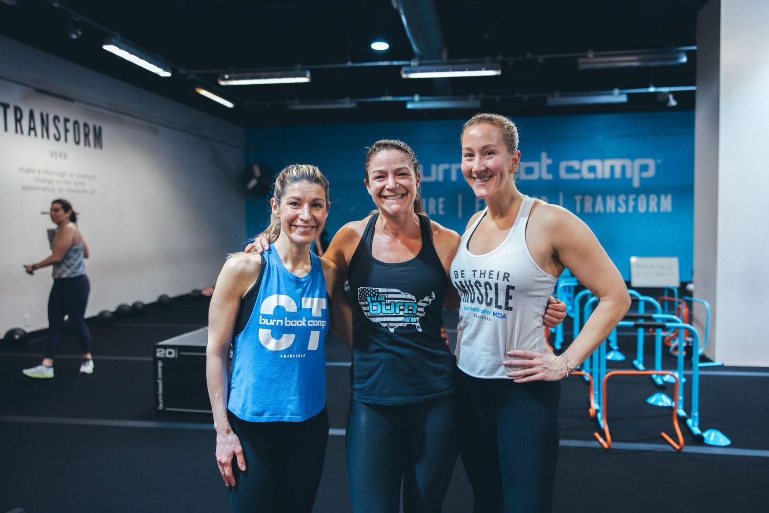 Three fitness enthusiasts in workout gear posing together at a modern gym facility.
