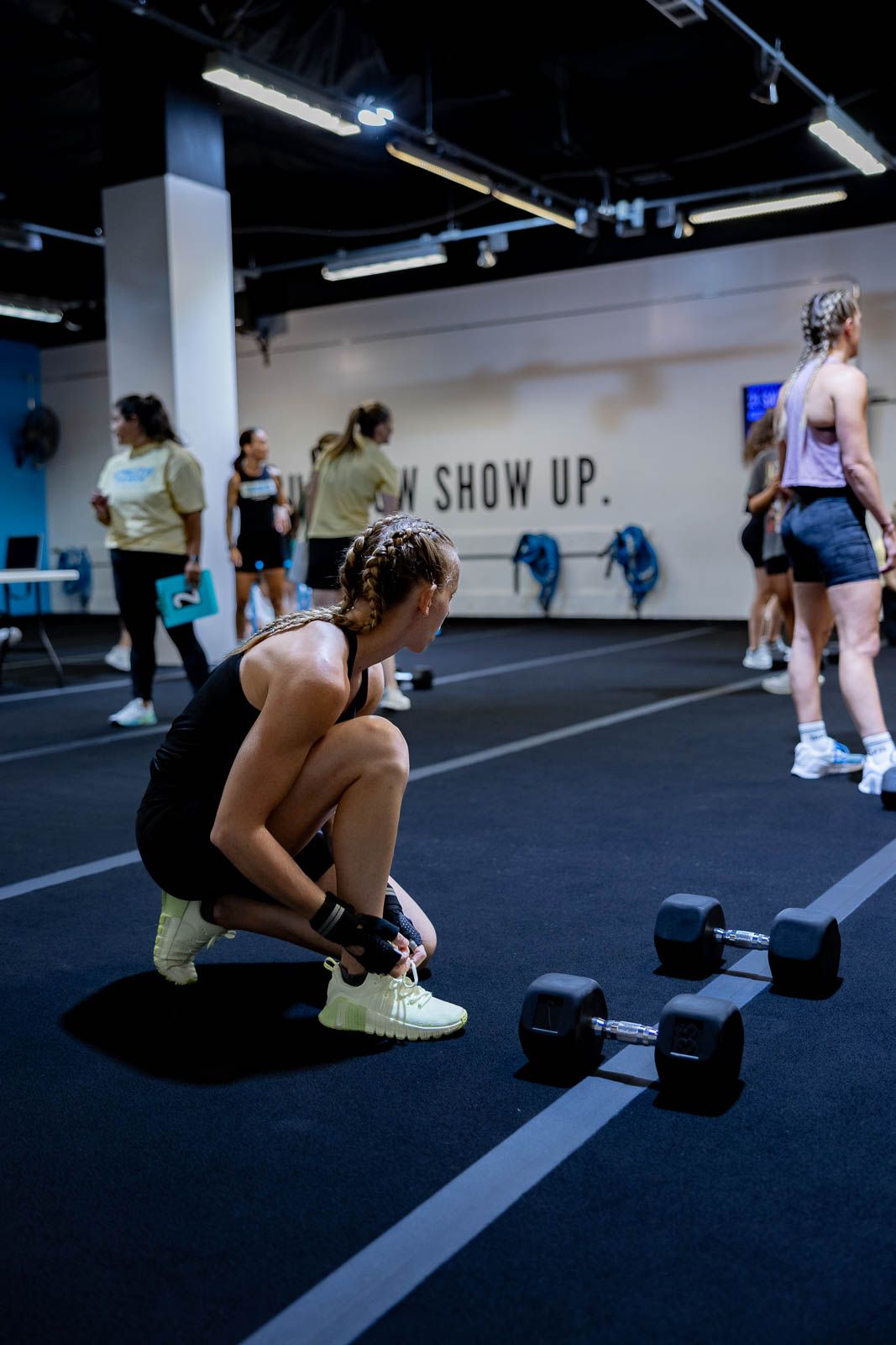 Athletes workout with dumbbells at modern gym with 'SHOW UP' text visible on wall.