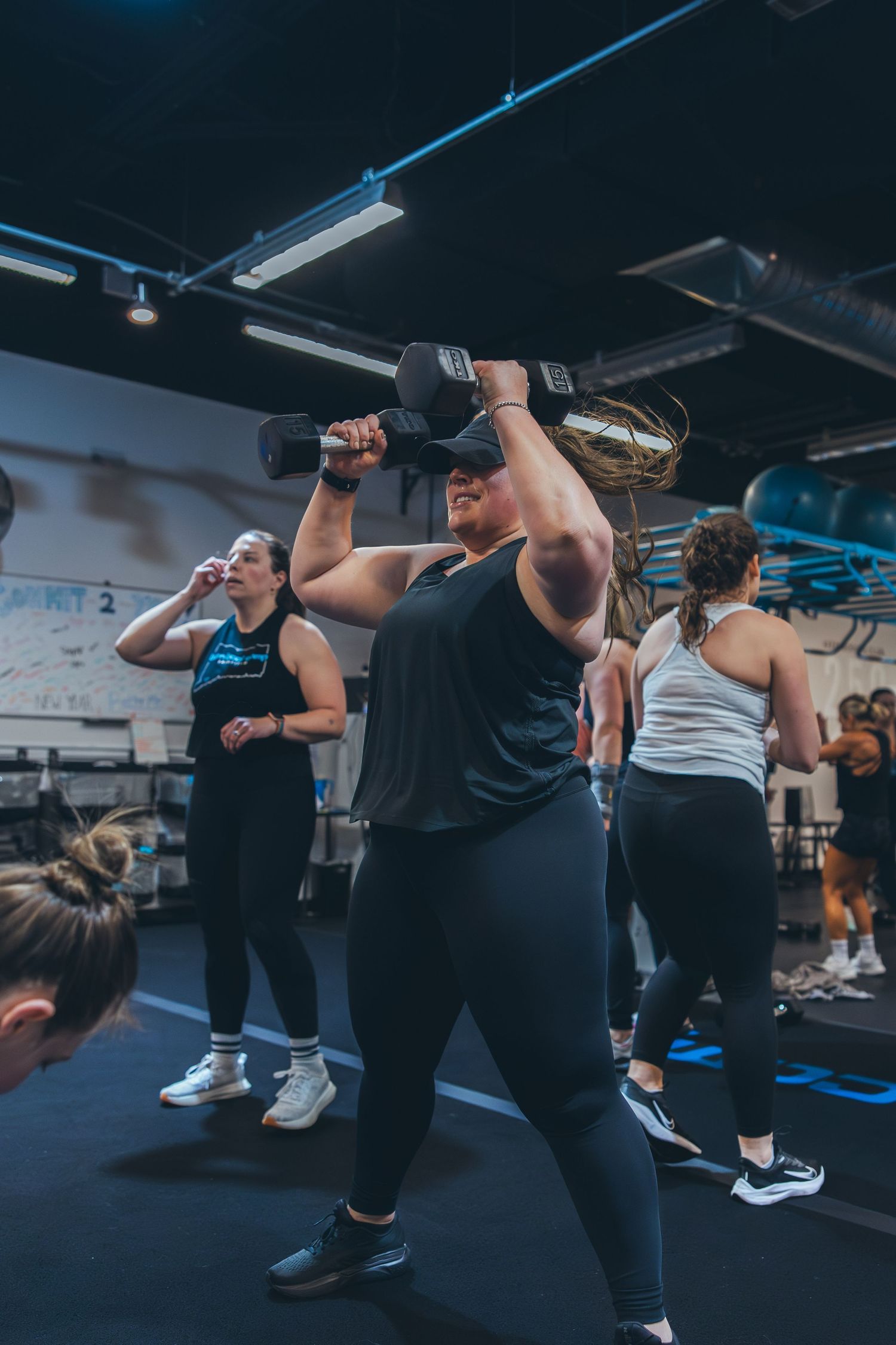 Fitness participants performing overhead dumbbell exercises during a group workout class.