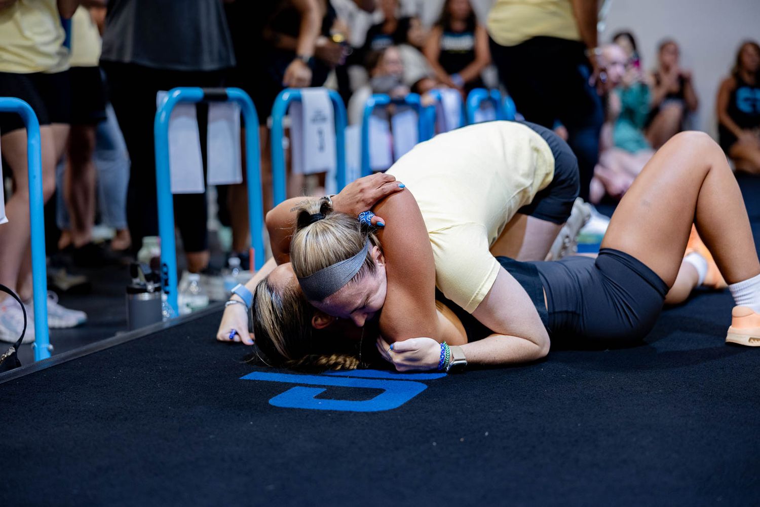Athletes perform an intense workout on black mats during a competitive fitness event.