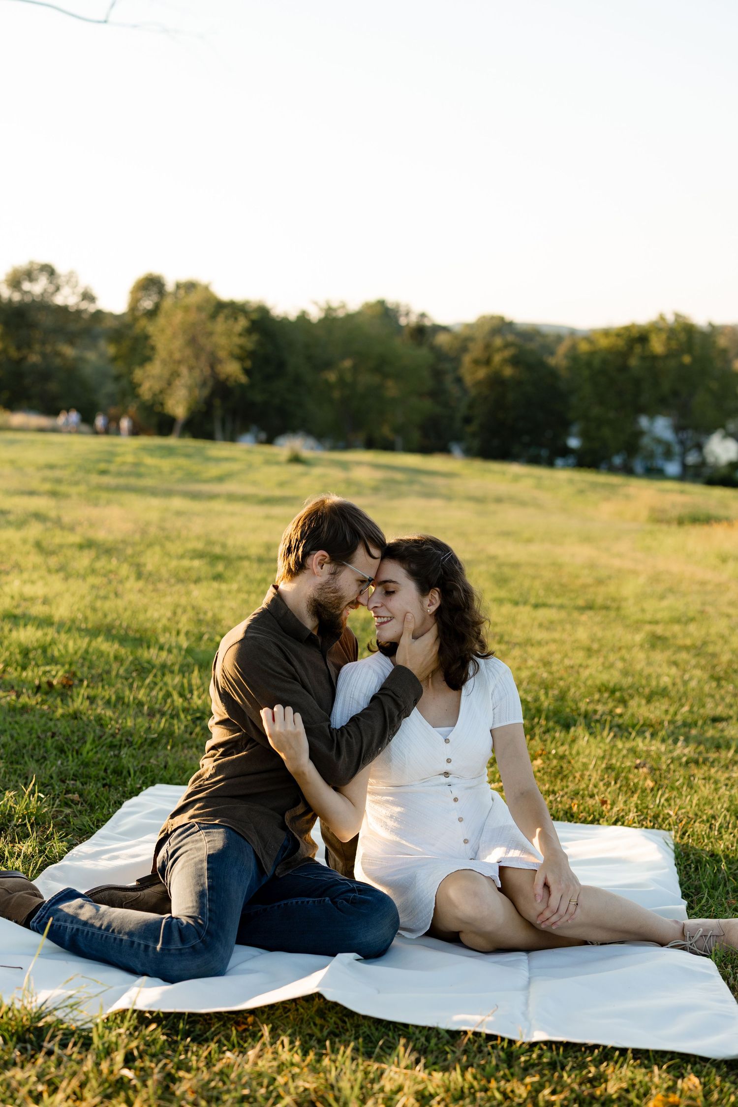 Couple sharing an intimate moment while sitting on a blanket in a sunny meadow at golden hour.