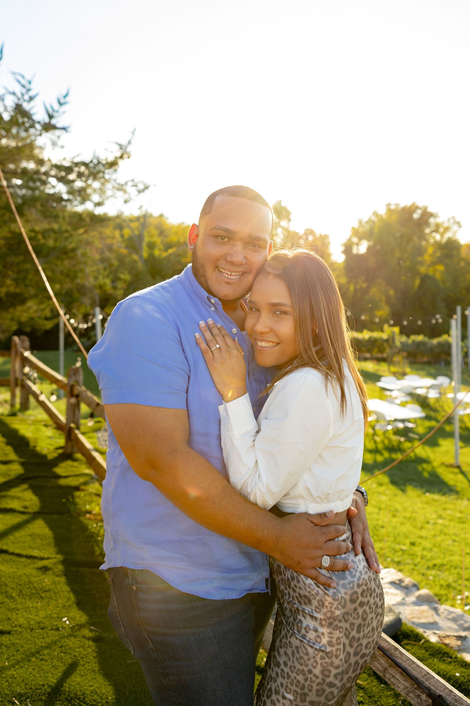 A couple embraces outdoors during golden hour in a grassy park setting.