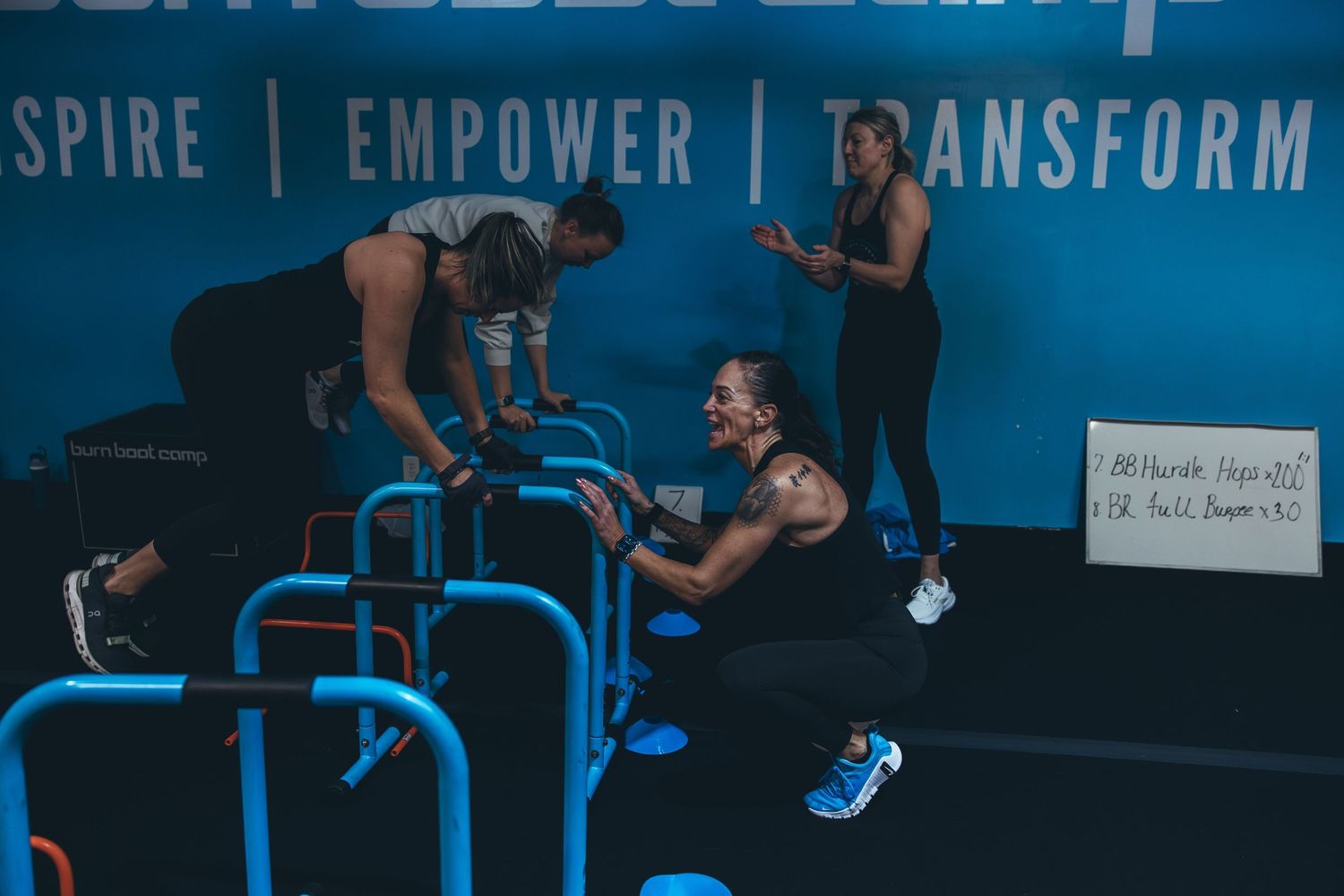 Group workout session focusing on dips and bodyweight exercises at a fitness studio with blue wall signage.