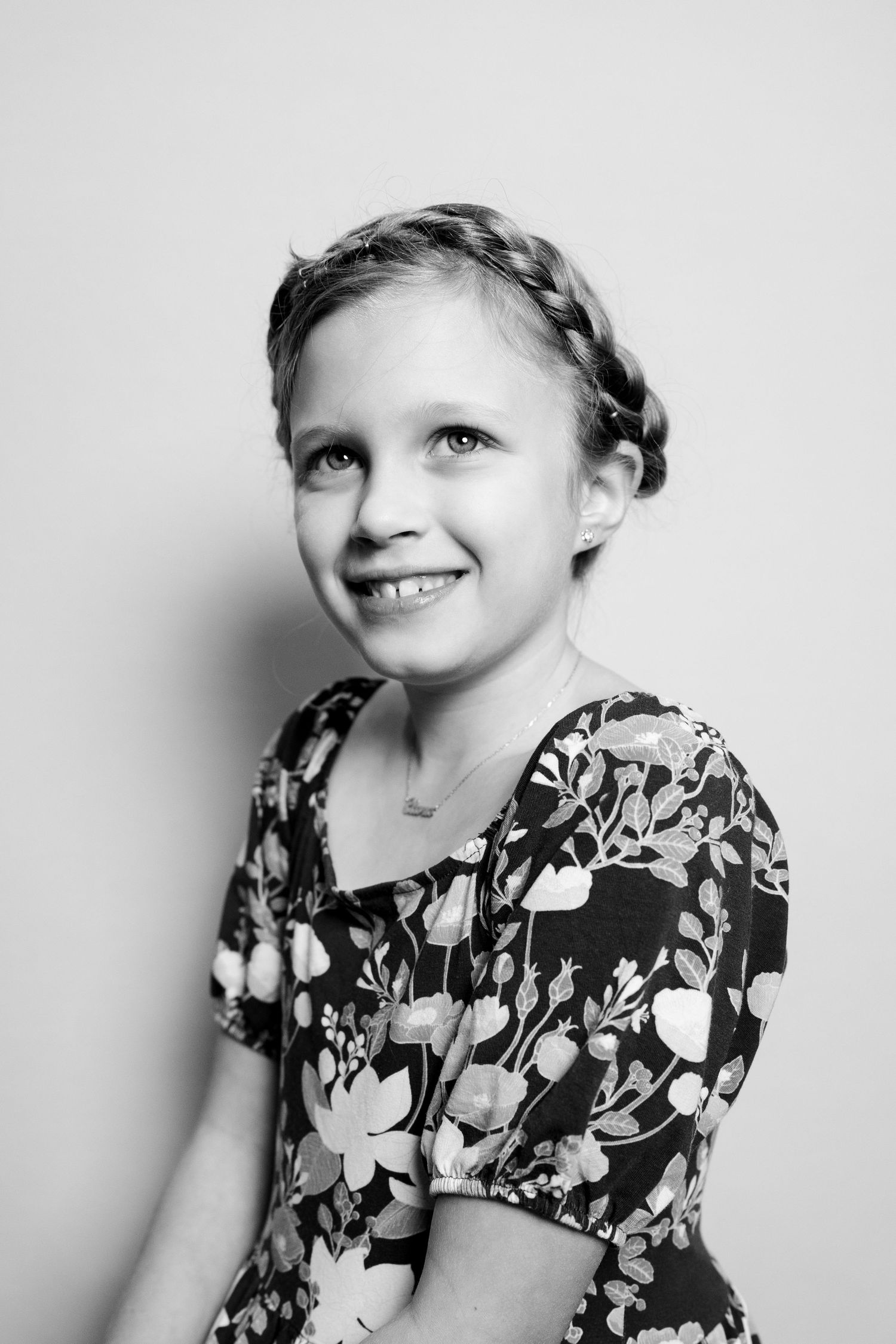 Black and white portrait of a young child with braided hair wearing a floral dress and smiling.