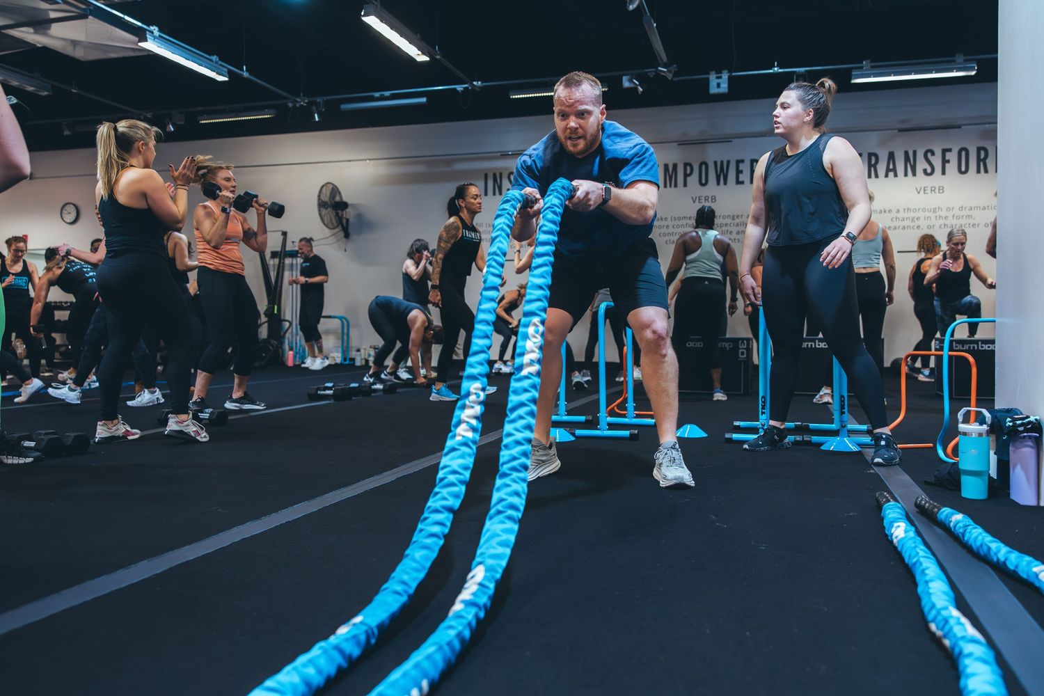 Participant performs battle rope exercises during a high-intensity workout in a modern fitness facility.
