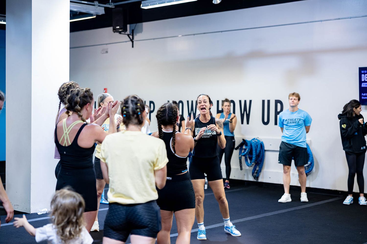Group fitness class participants doing burpee exercises on dark flooring in a modern gym facility.