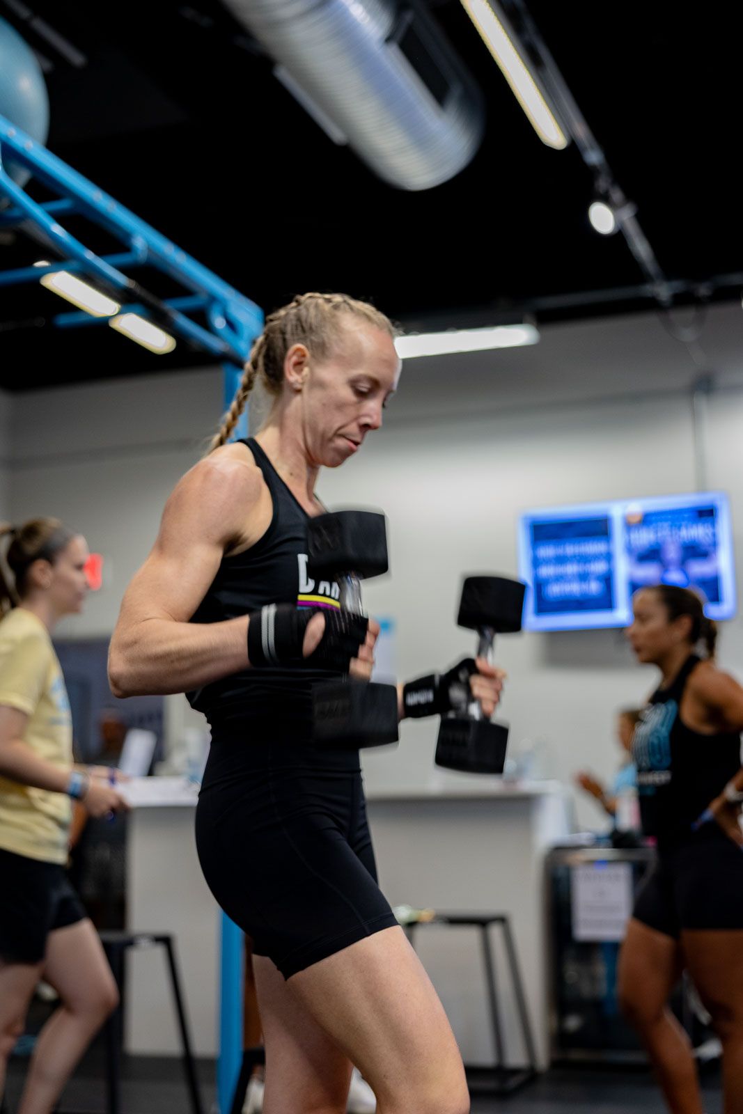 Athlete in black workout attire performing dumbbell exercises during an indoor training session.