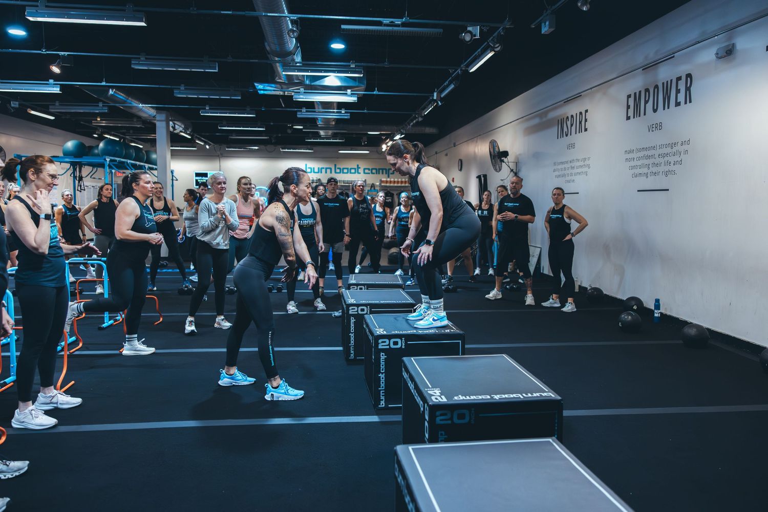Group fitness class participants exercising in a modern gym with black floors and white walls.